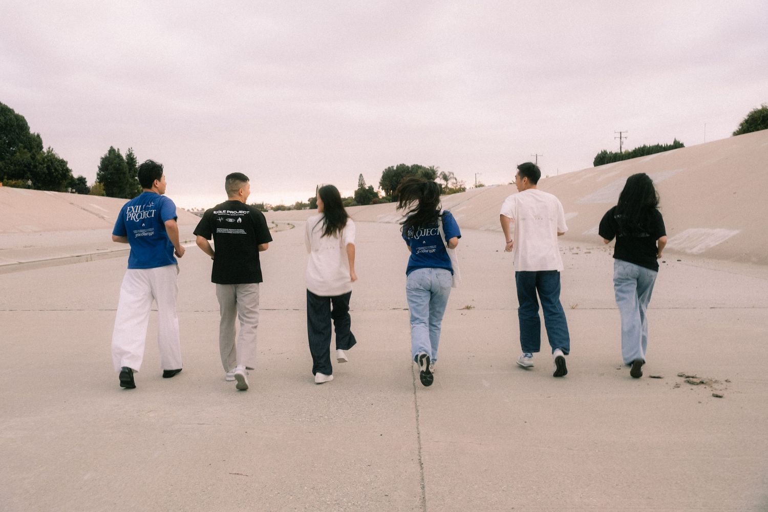 Group of six people walking away in casual streetwear on a concrete outdoor surface.