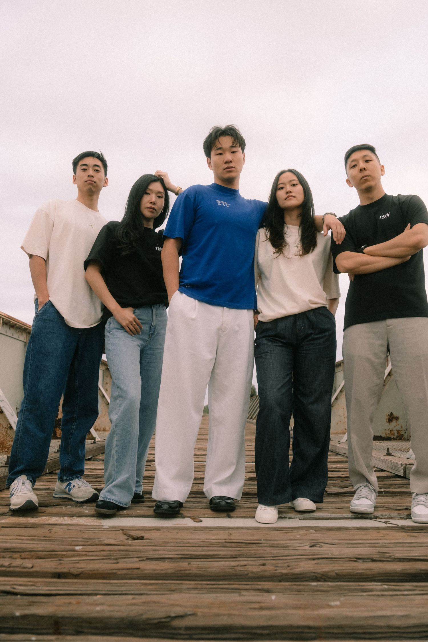 Five young Asian adults in casual streetwear posing together on a wooden rooftop platform.