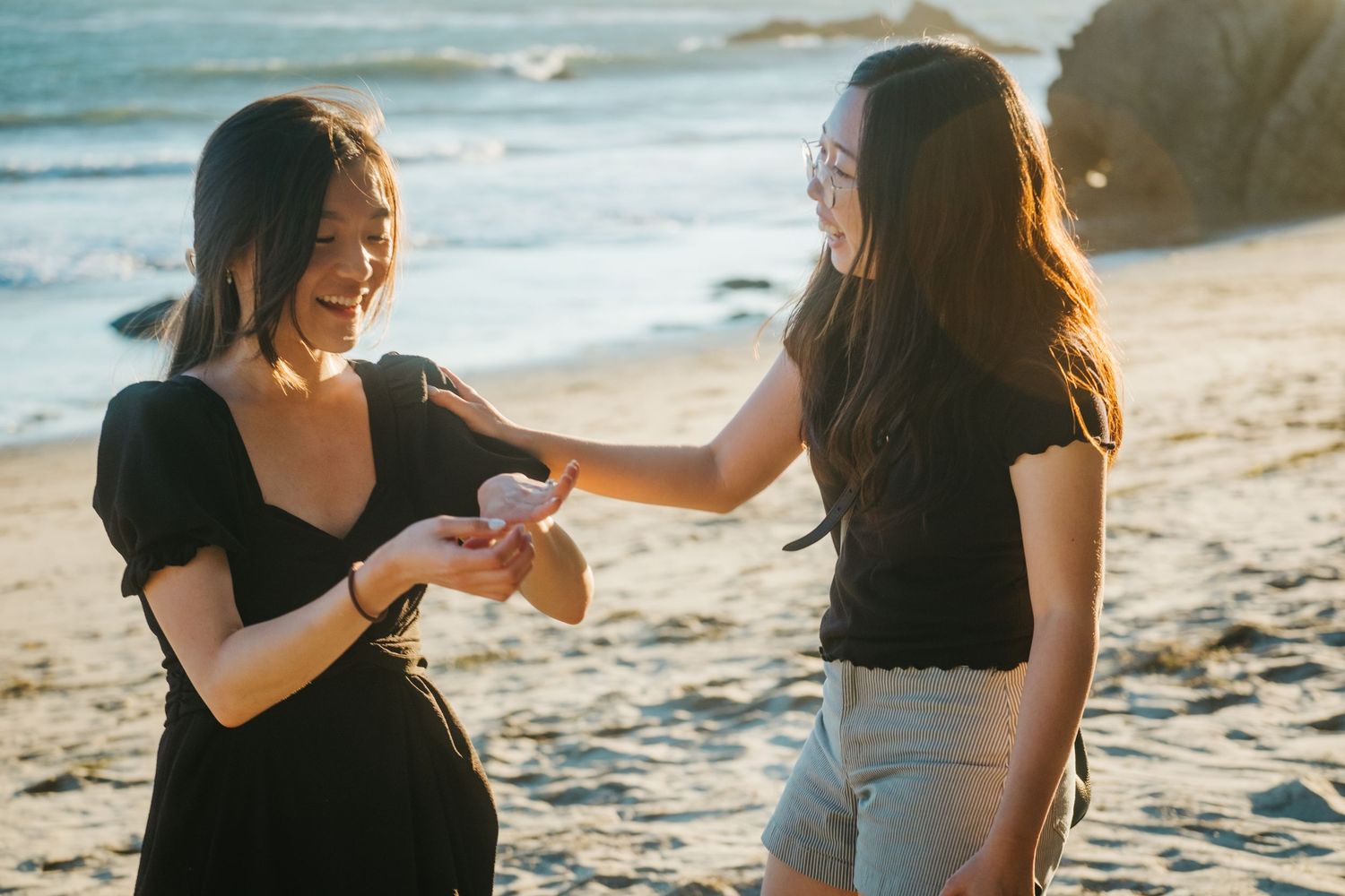 Two women laughing and sharing a moment on a sunny beach.