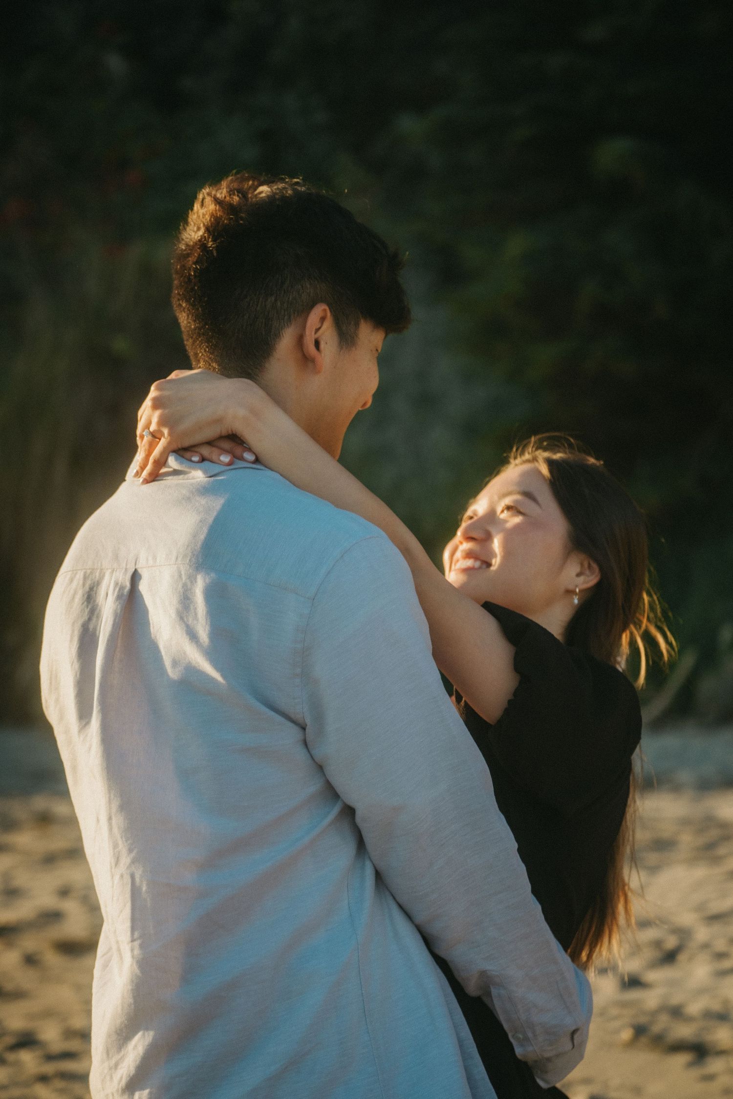 Happy couple embracing on a sandy beach at golden hour, woman smiling joyfully at partner.