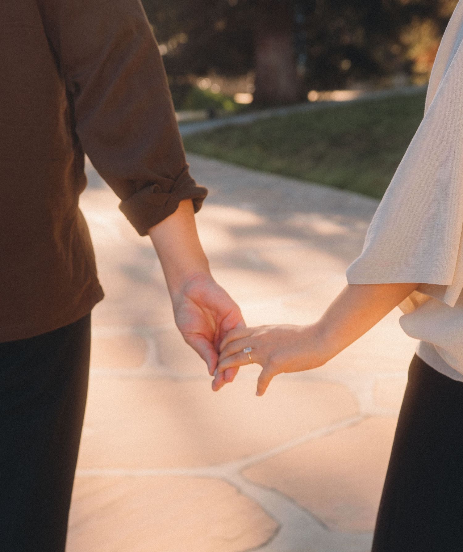 Engaged couple holding hands while walking outdoors, showcasing a gold diamond engagement ring.