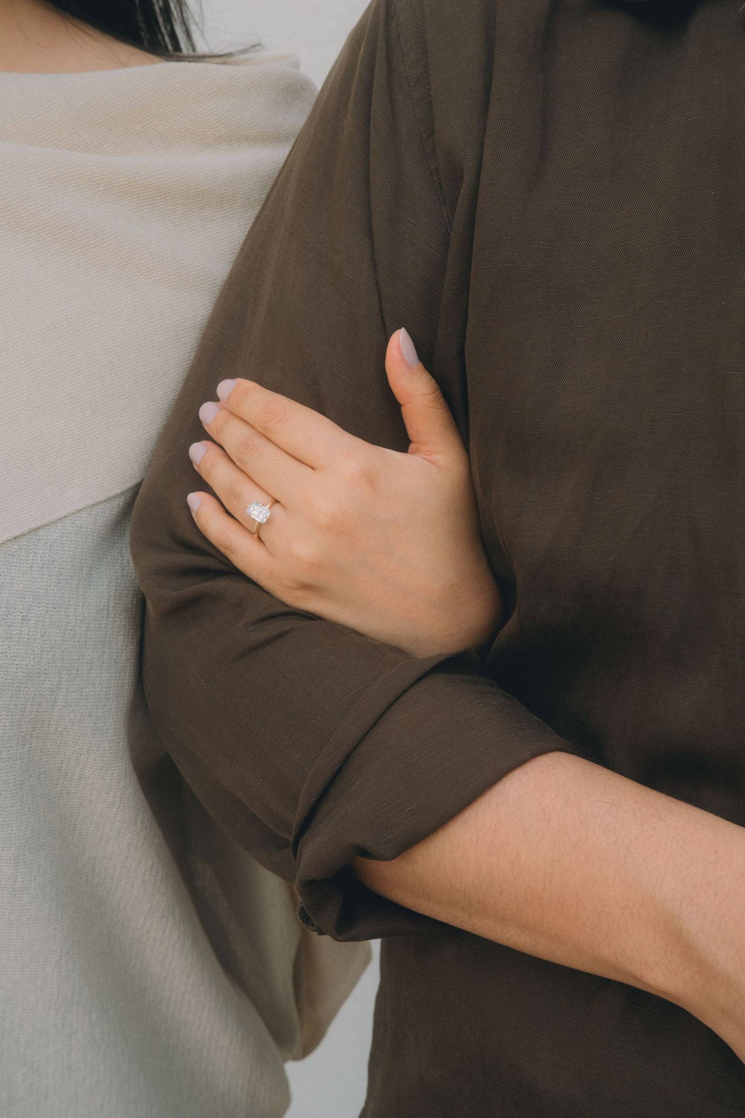 Close-up of a woman's hand wearing a pearl ring gently holding a man's arm in a brown jacket.