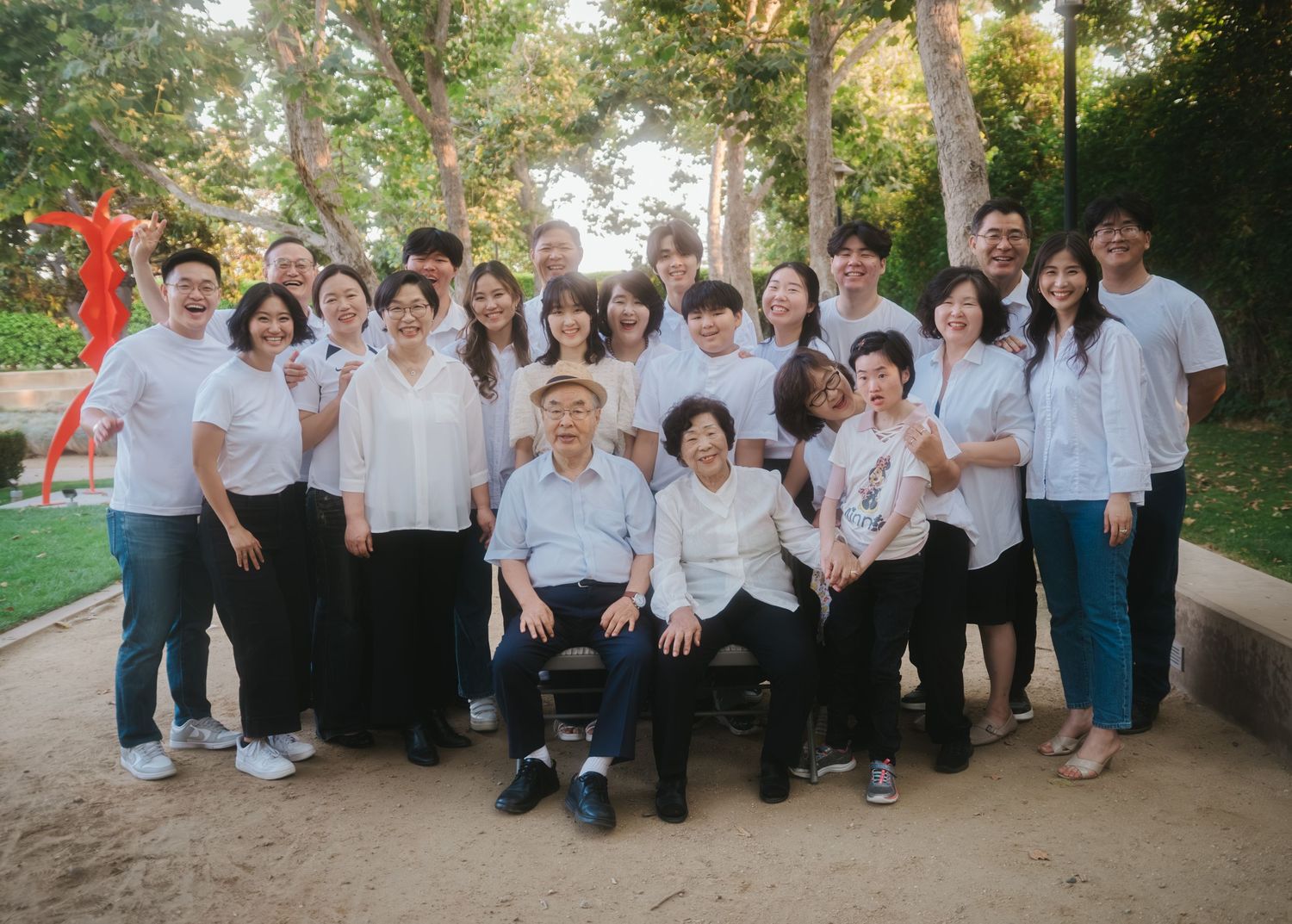 Large Asian family group photo outdoors, wearing white shirts, posing together with elderly couple seated in center.