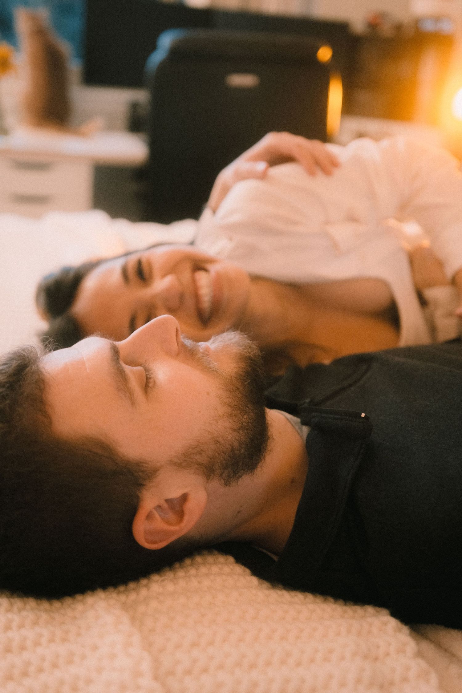 A happy couple lying on a bed together, smiling and relaxing in a warmly lit cozy room.