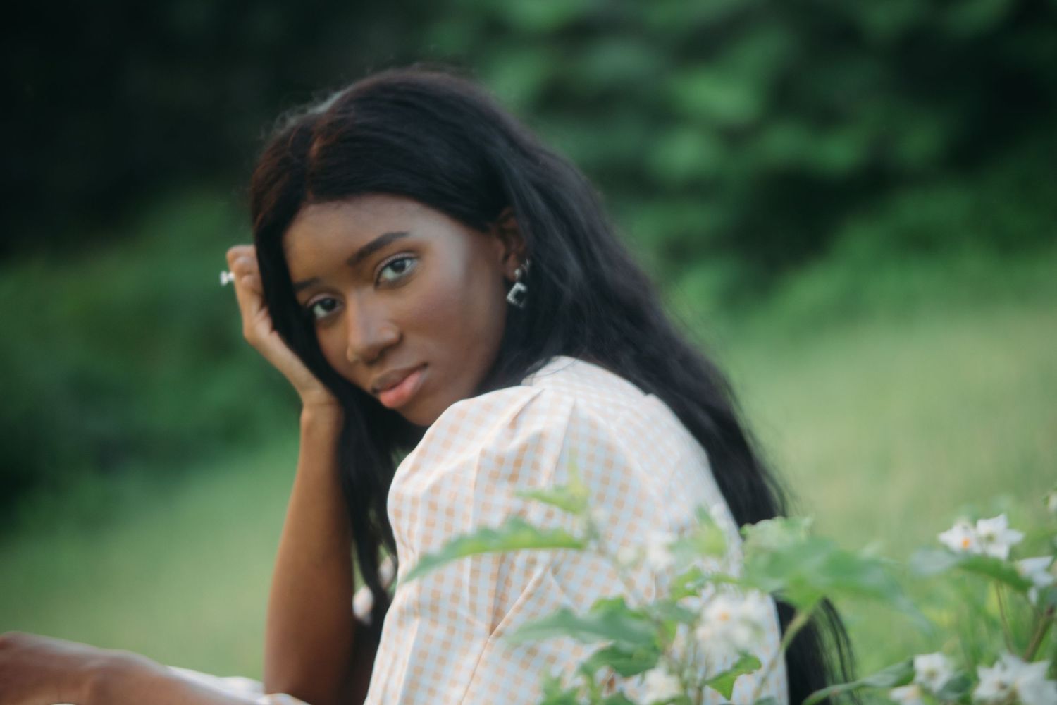 Close-up portrait of young Black woman in plaid dress near white wildflowers.