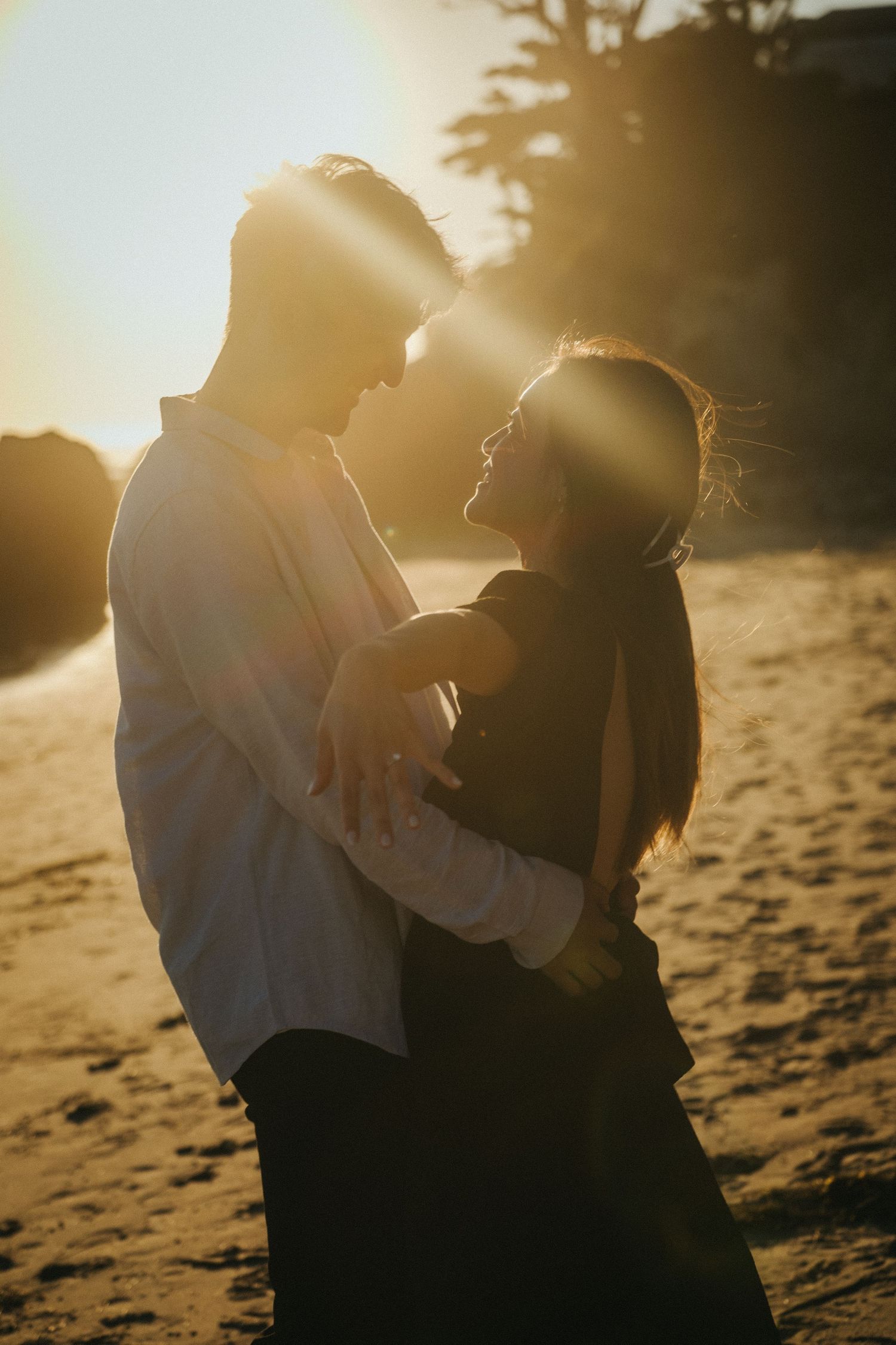 Couple embracing on beach at golden sunset with warm lens flare.