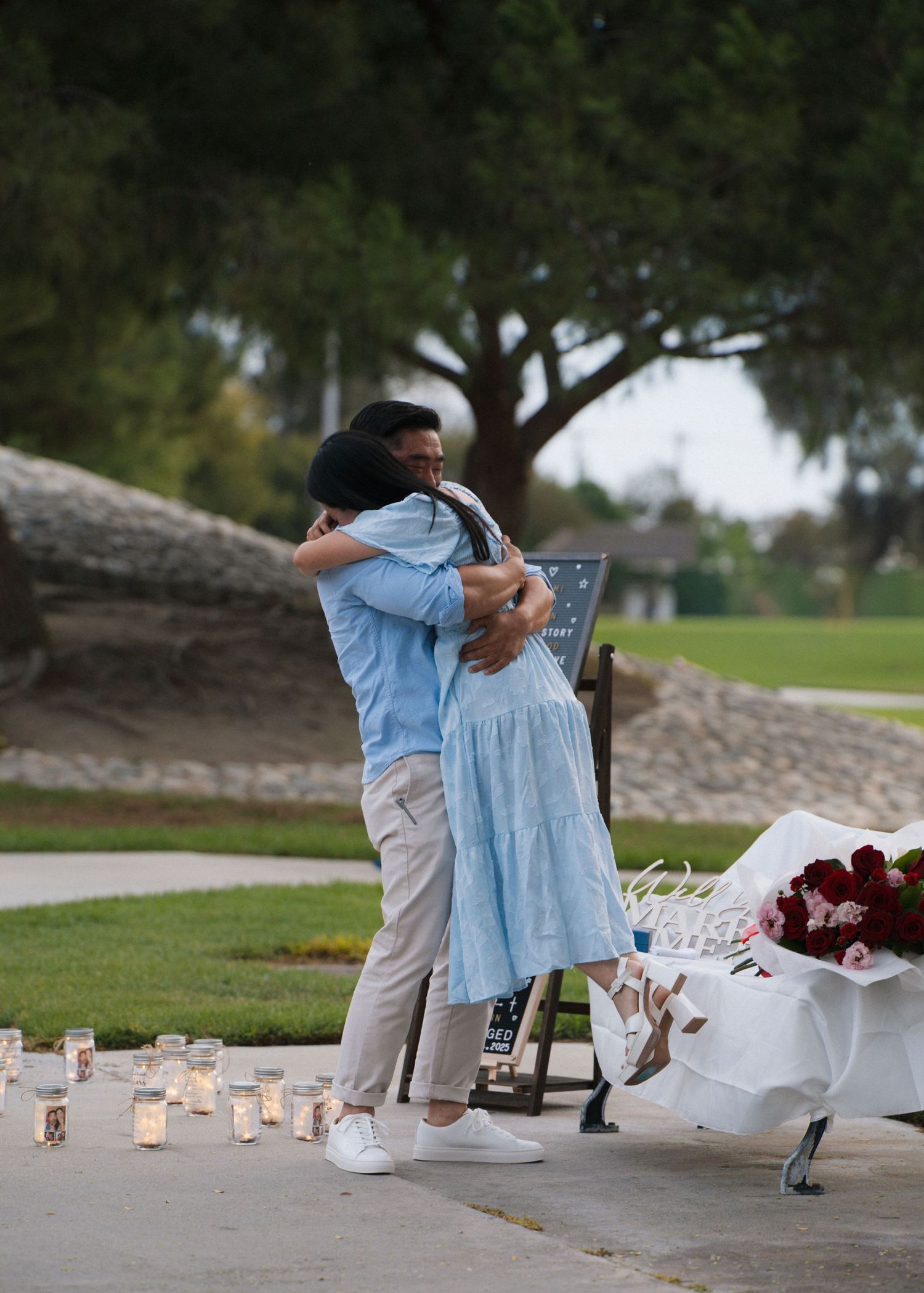 Couple embracing during romantic candlelit proposal at dusk with floral arrangement nearby.