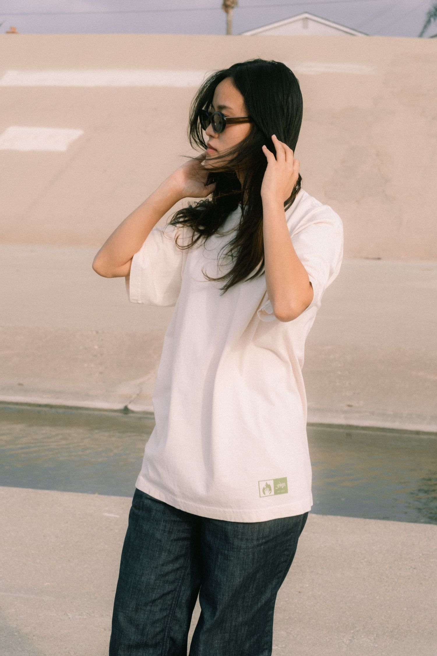 Woman in oversized white t-shirt and dark jeans wearing sunglasses outdoors.