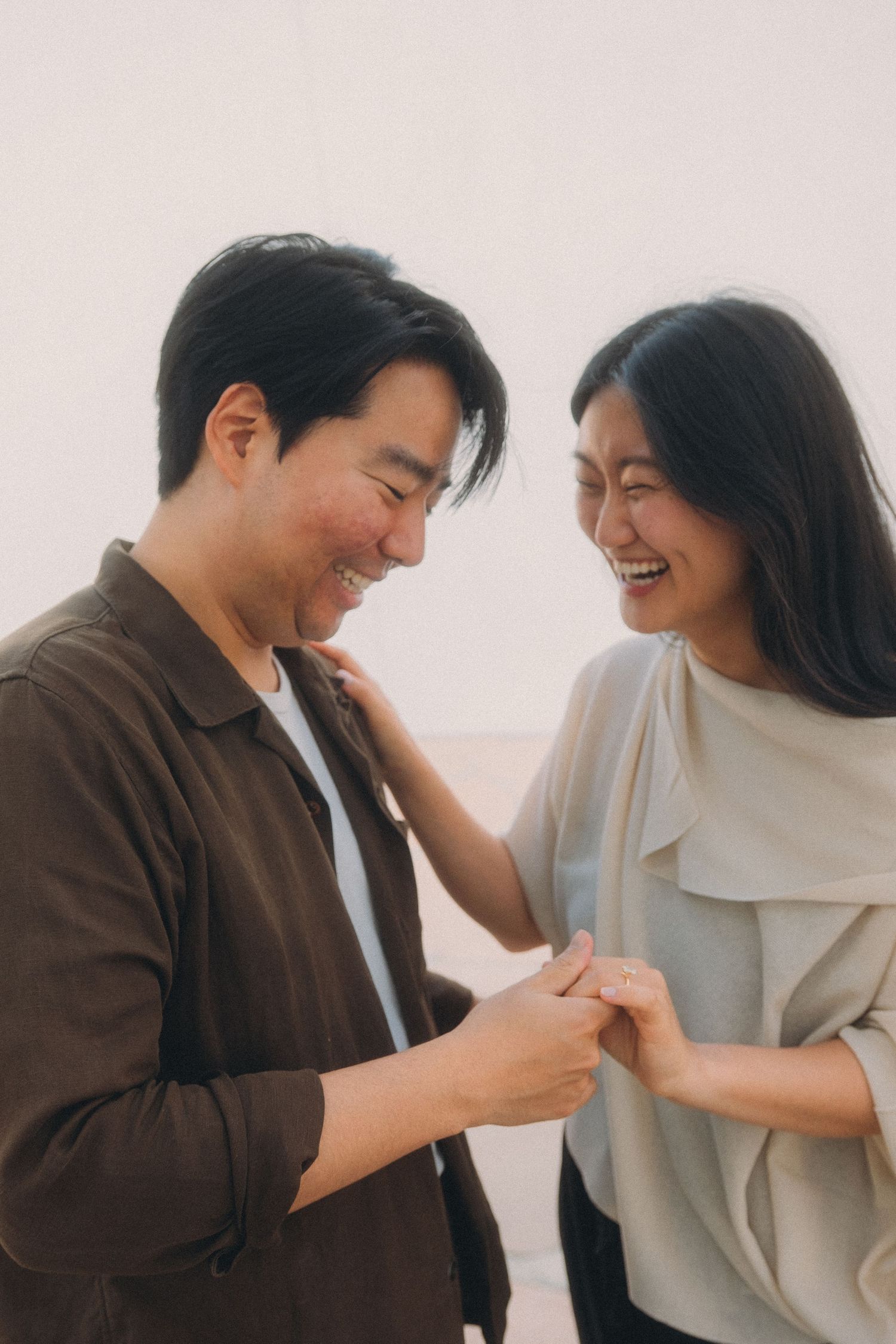 Happy Asian couple laughs and holds hands together in a bright outdoor setting.