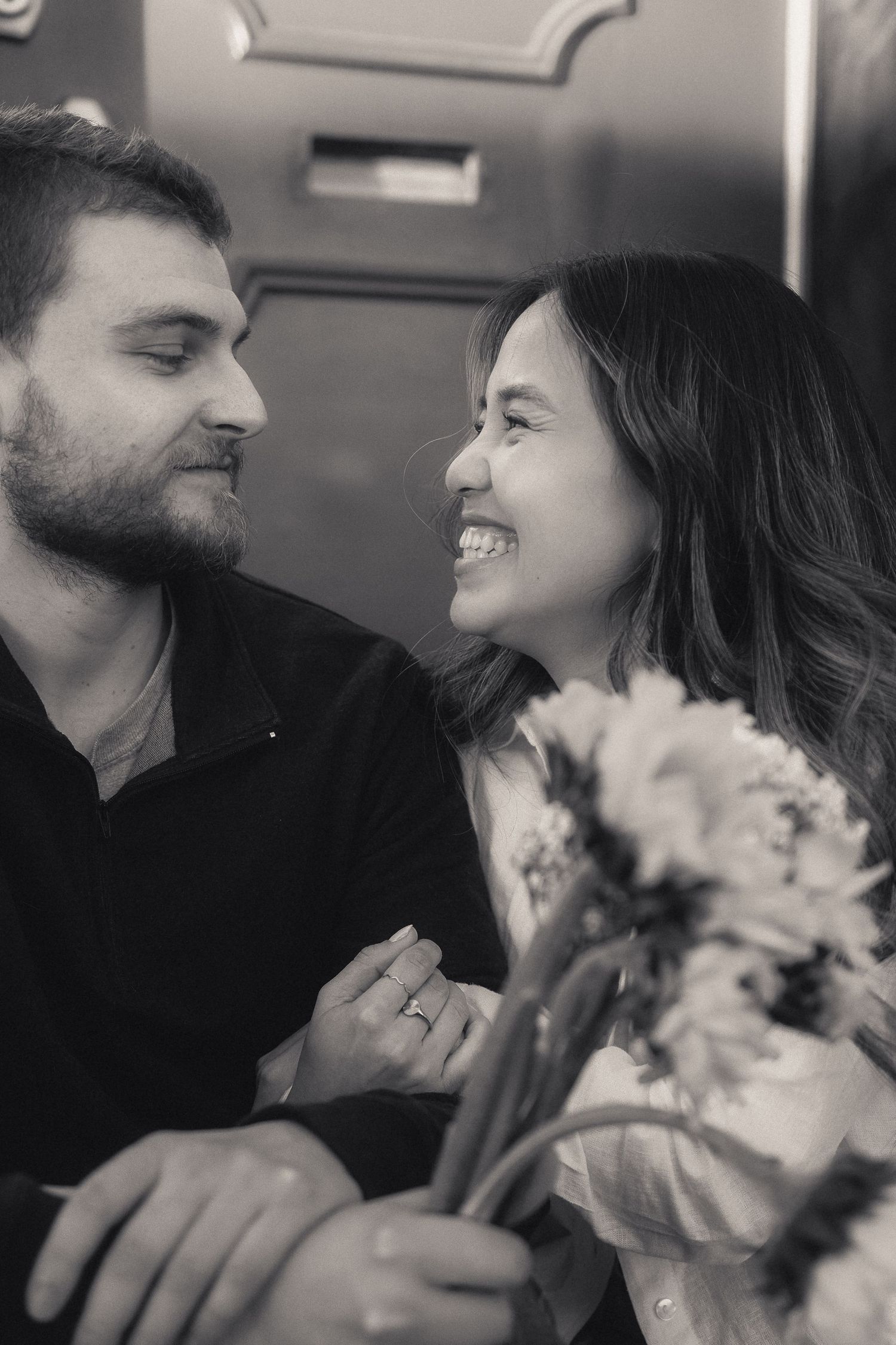 Black and white photo of a smiling couple holding flowers, gazing at each other romantically.