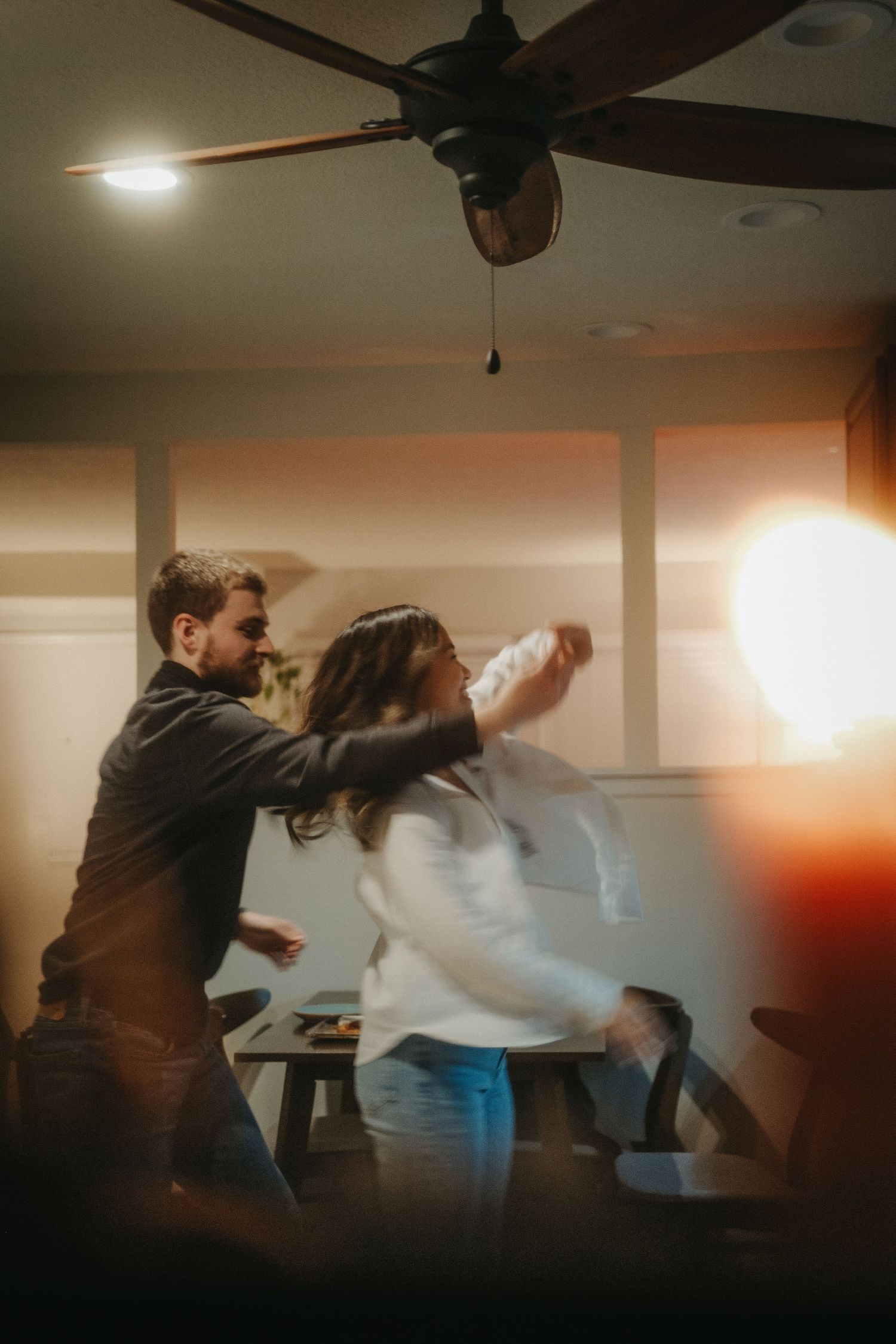 Couple dancing together in a warmly lit room with a ceiling fan overhead, captured with a dreamy motion blur effect.