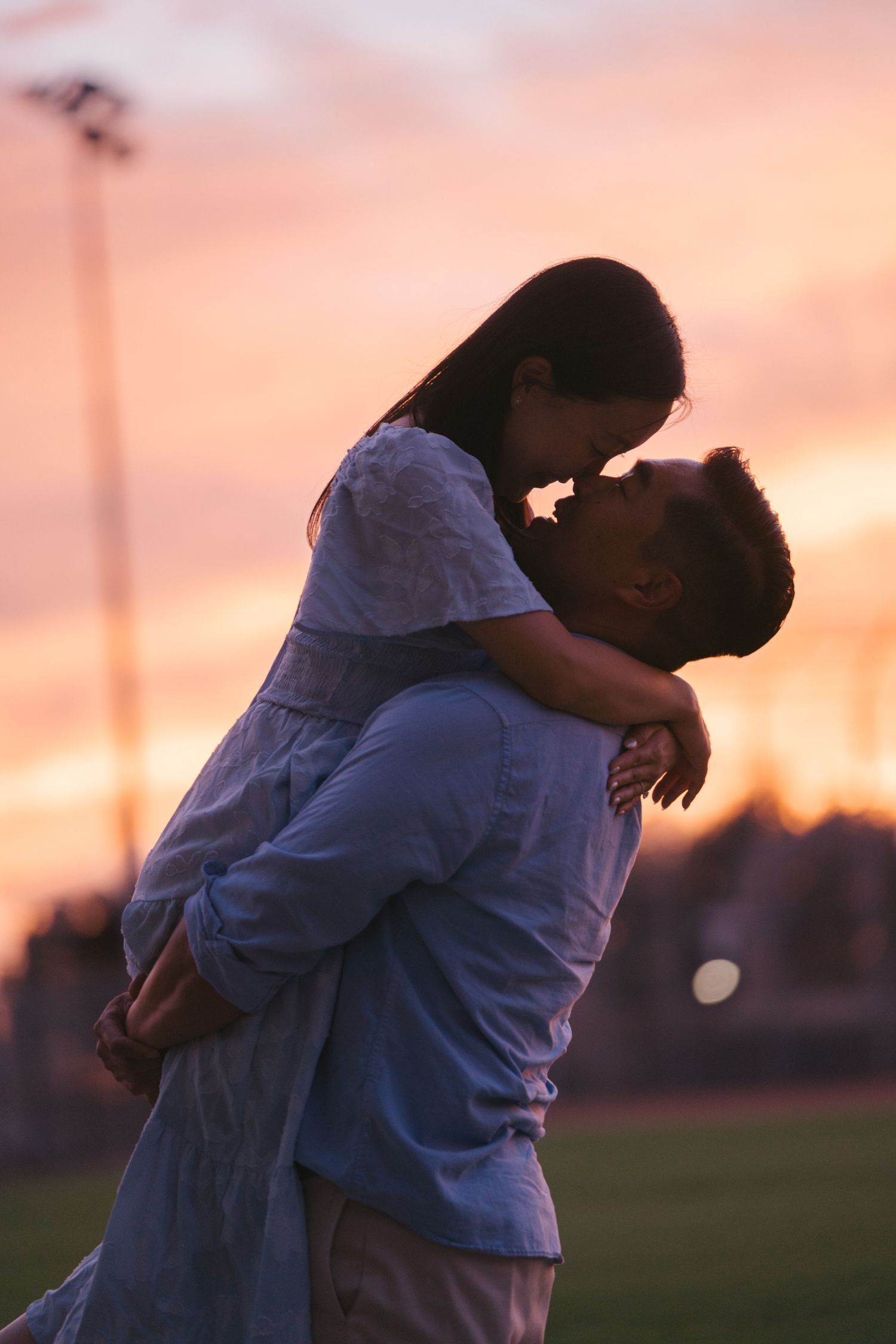 Romantic couple sharing an intimate moment at sunset, man lifting woman against a vibrant pink sky.