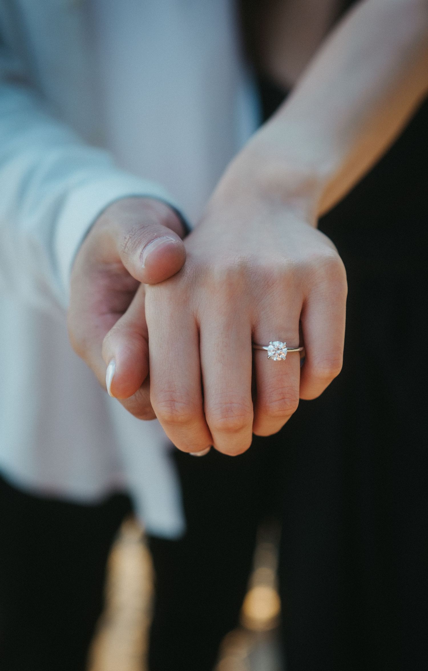 Close-up of a couple holding hands showing off a sparkling solitaire diamond engagement ring.
