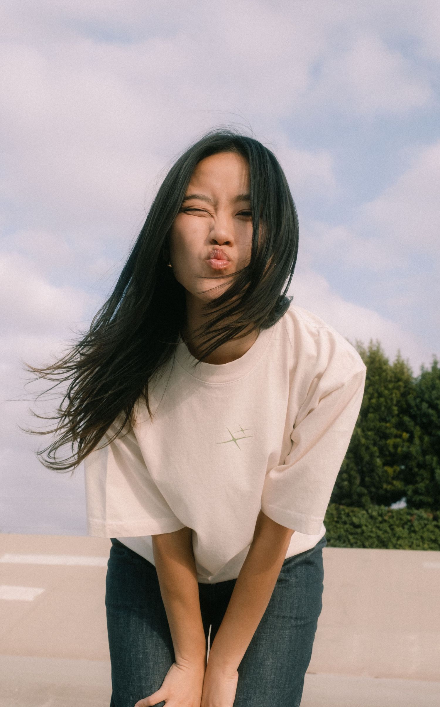 Young Asian woman in white t-shirt and jeans making a pouty face outdoors on a cloudy day.