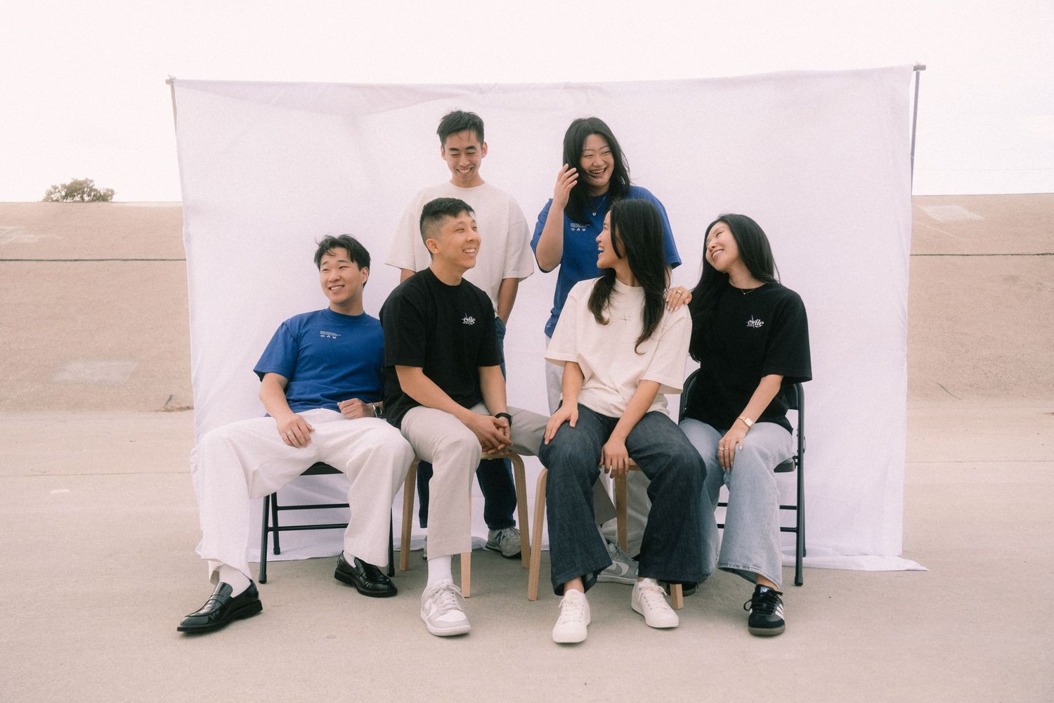 Group of six young people posing together in Exile Project t-shirts outdoors on a rooftop.