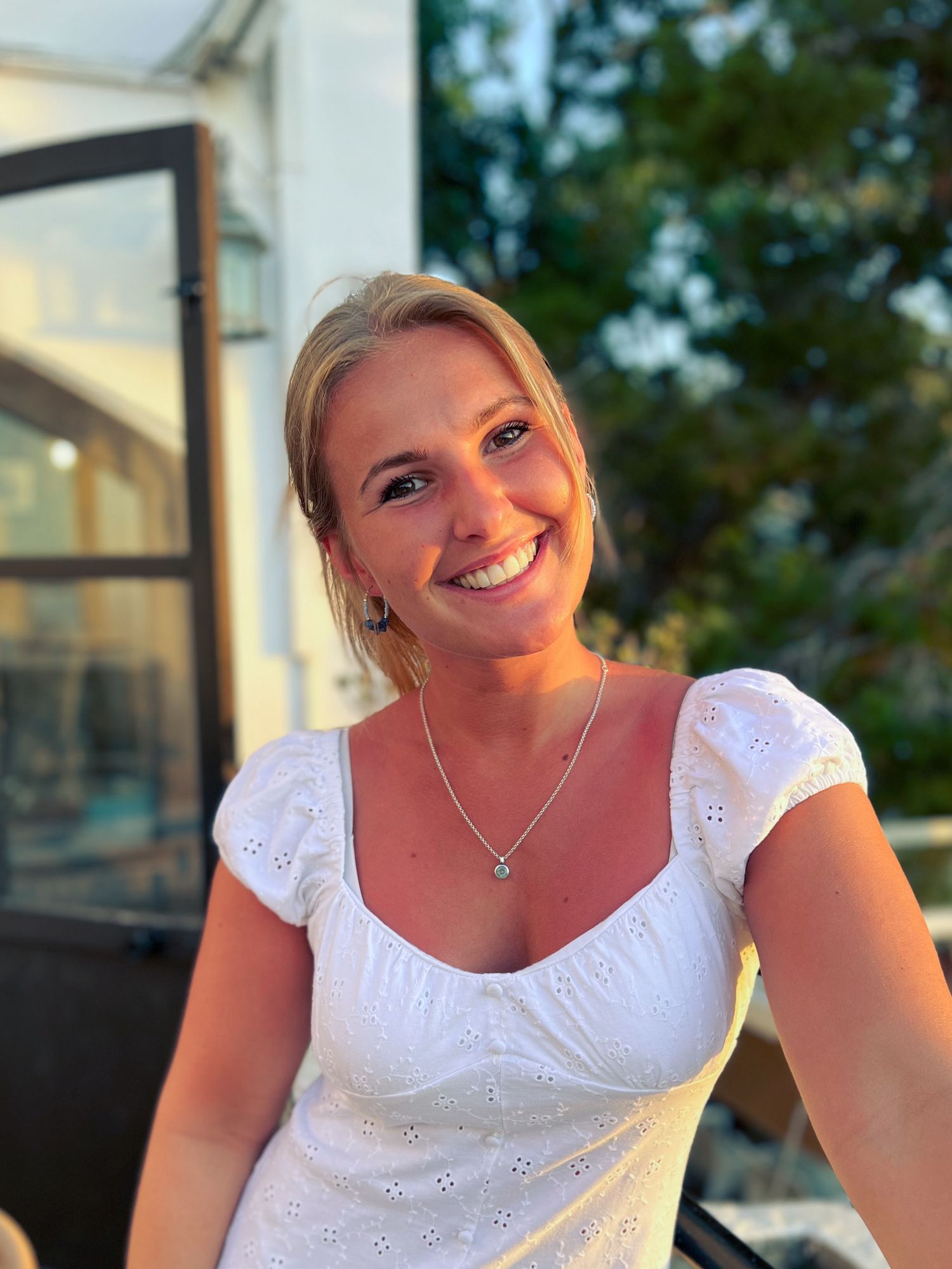 Beautiful blonde woman in white puff-sleeve dress smiling warmly in soft evening sunlight.