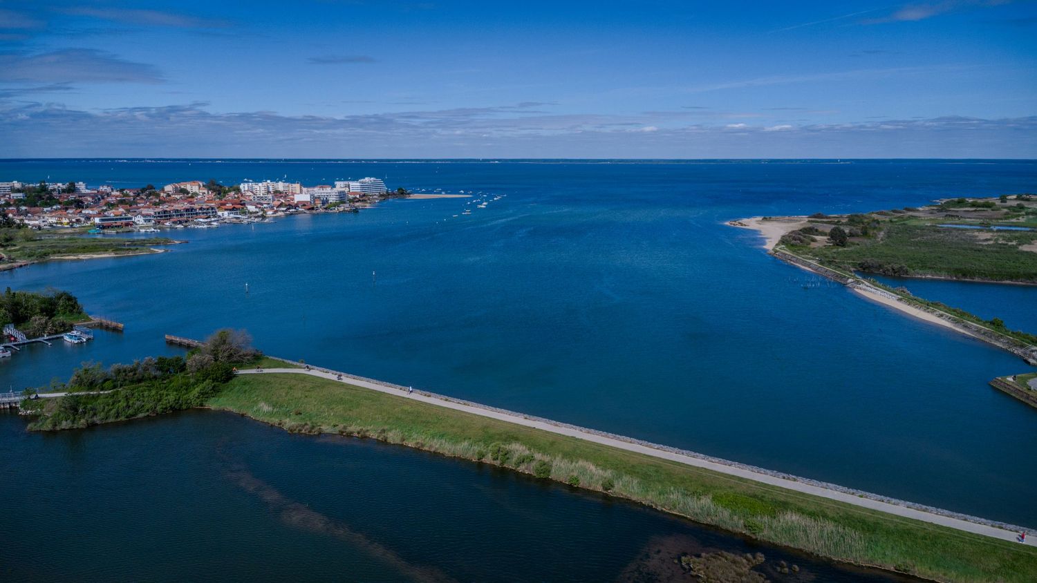Aerial view of a coastal town with blue ocean waters, green peninsula, and a road stretching along the waterfront.