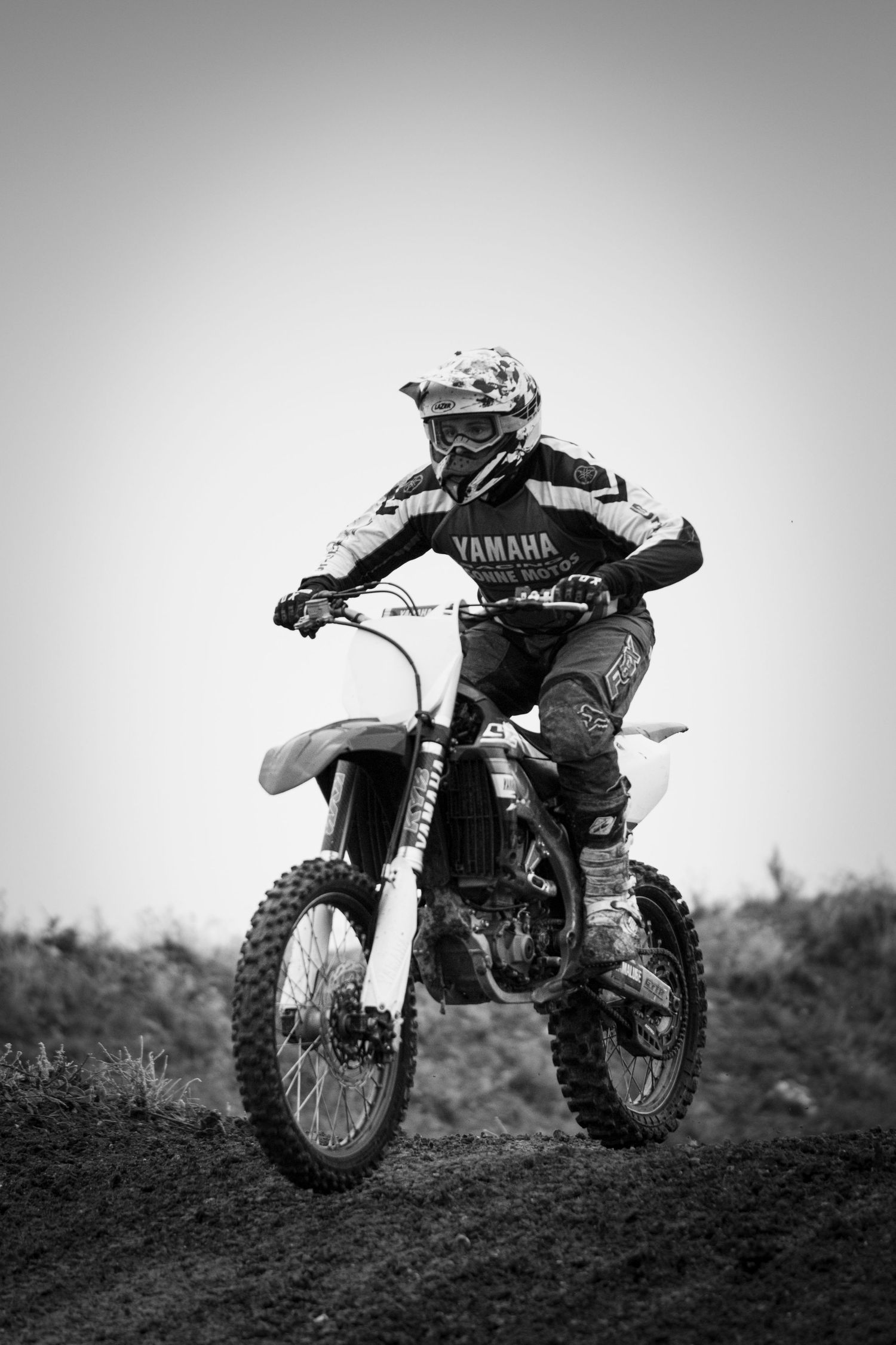 Black and white photo of a Yamaha motocross rider racing on a dirt track wearing full protective gear and helmet.