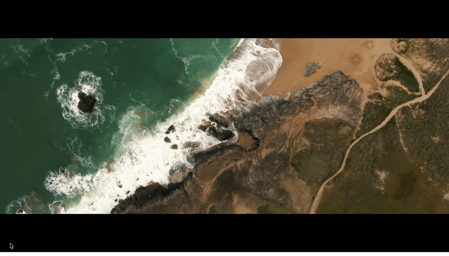 Aerial view of waves breaking along a sandy beach meeting rocky coastal terrain.
