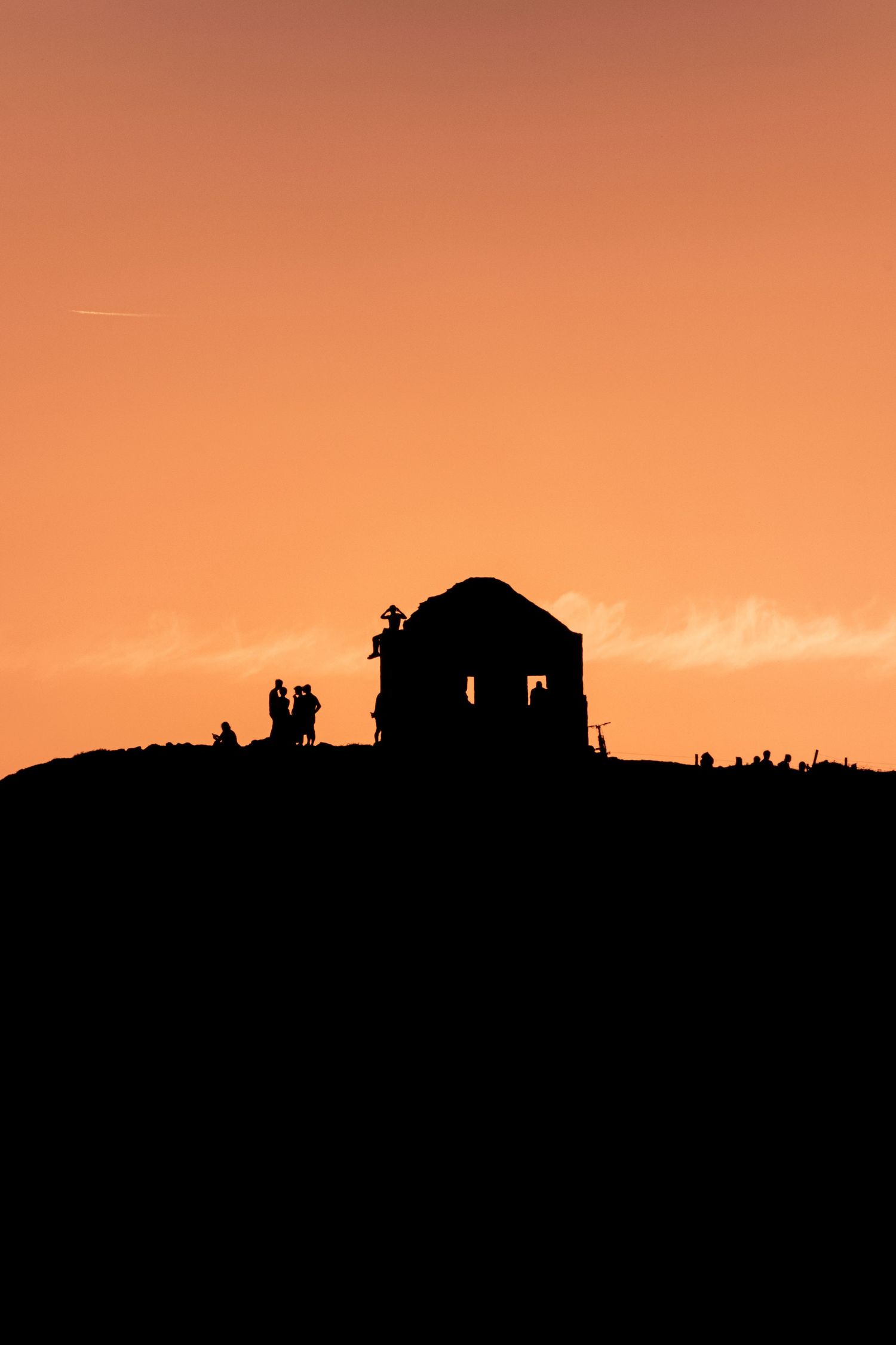 Silhouette of a historic building and people on a hilltop against a vivid orange sunset sky.