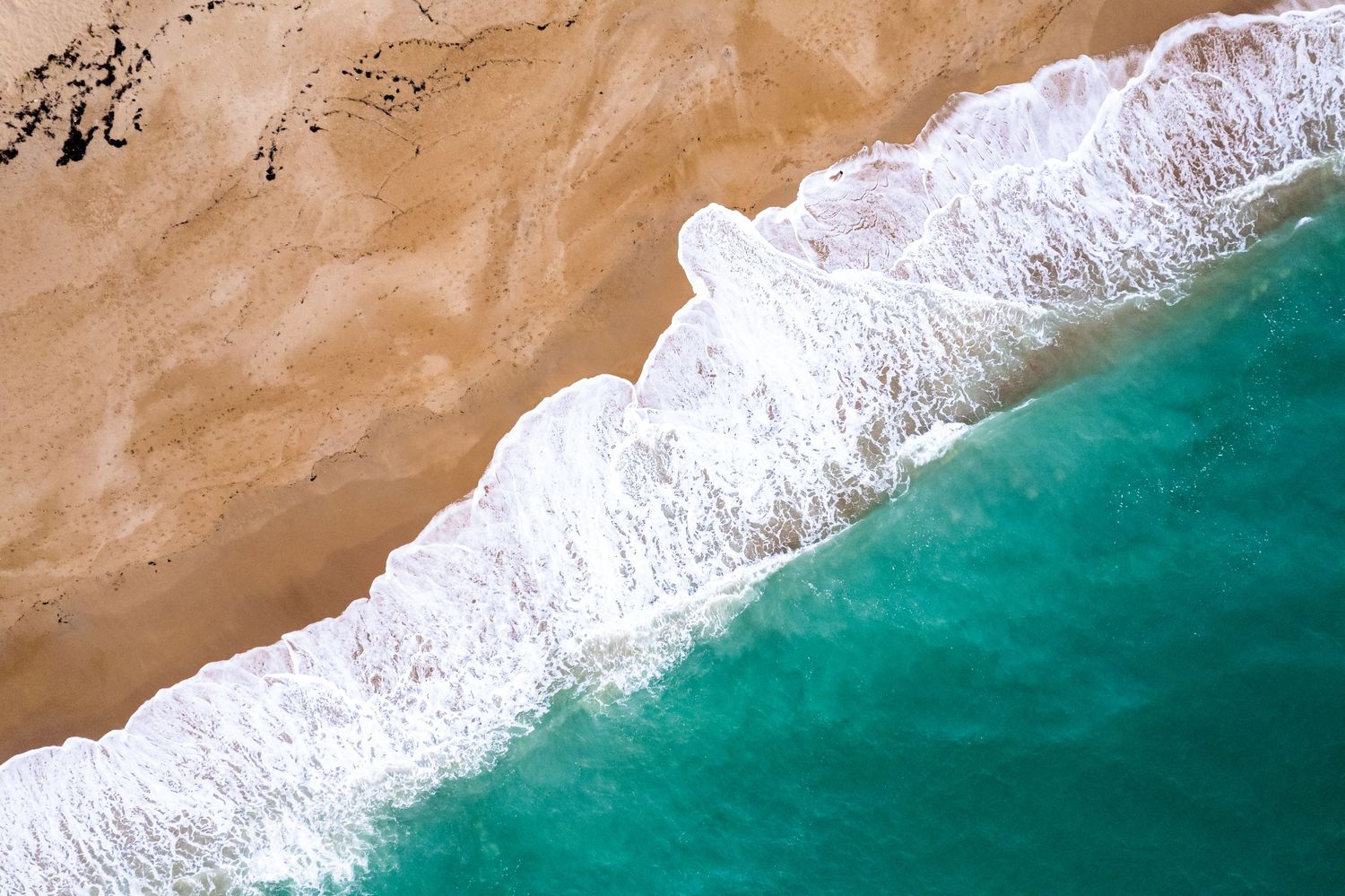 Aerial view of turquoise ocean waves washing onto a sandy beach shoreline.