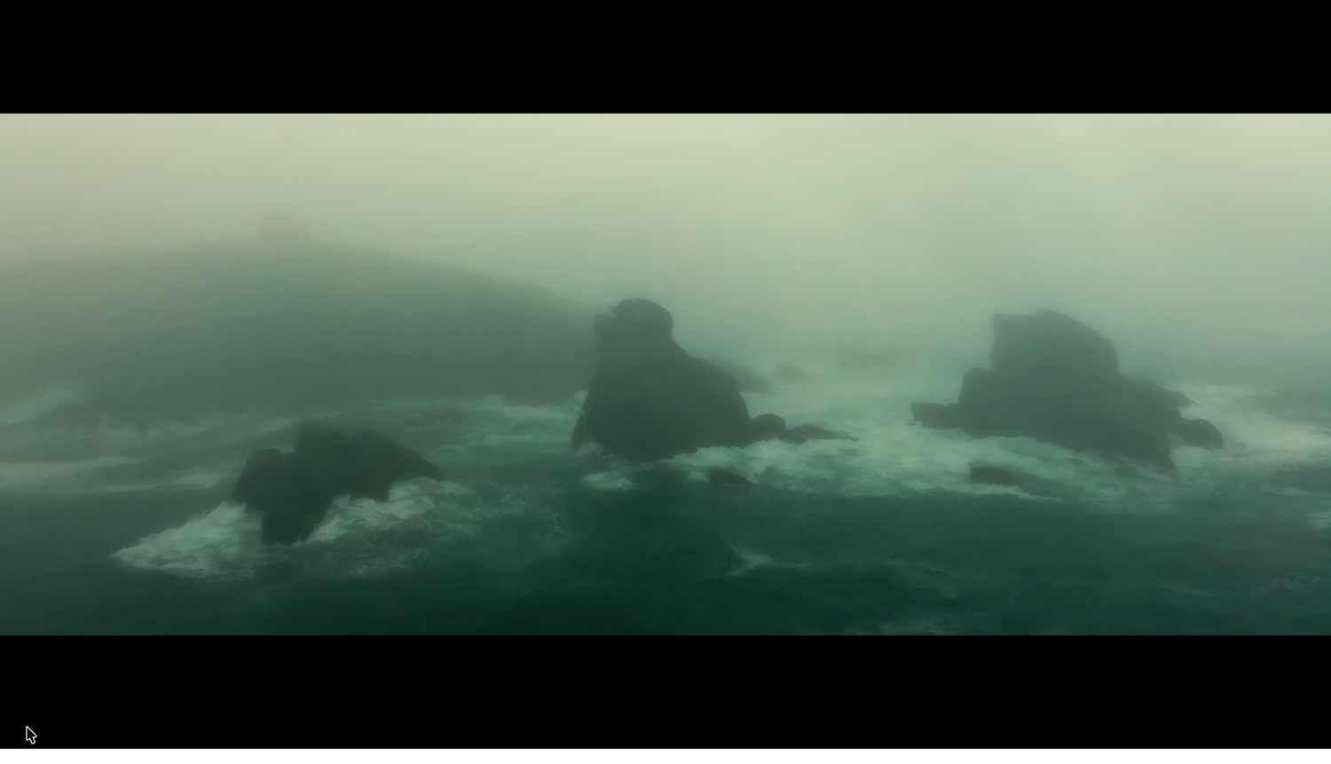 Misty foggy seascape with dark rocky outcrops emerging from turbulent ocean waters.