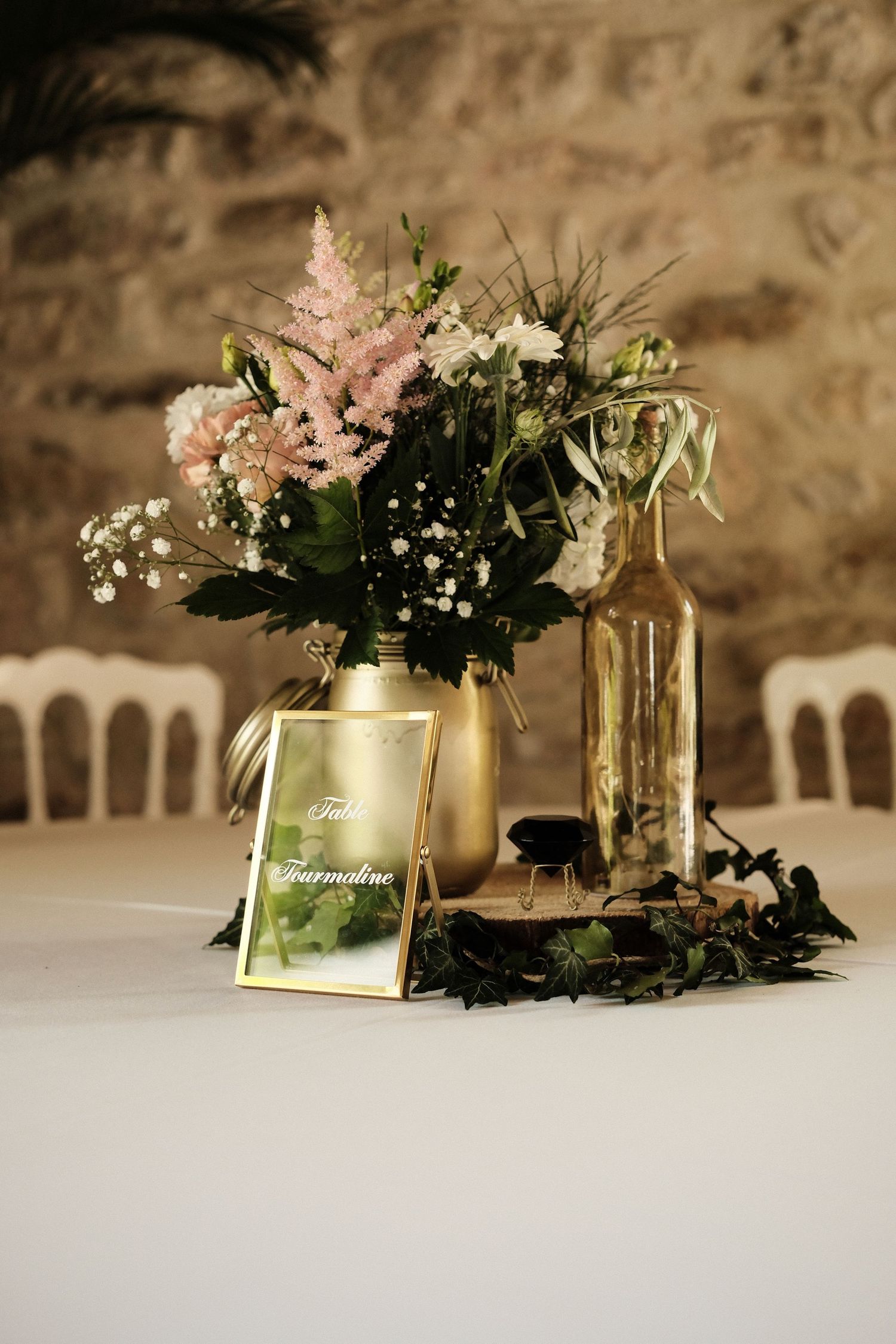 Elegant wedding table centerpiece featuring pink and white flowers in gold vases with a framed table name card on white linen.