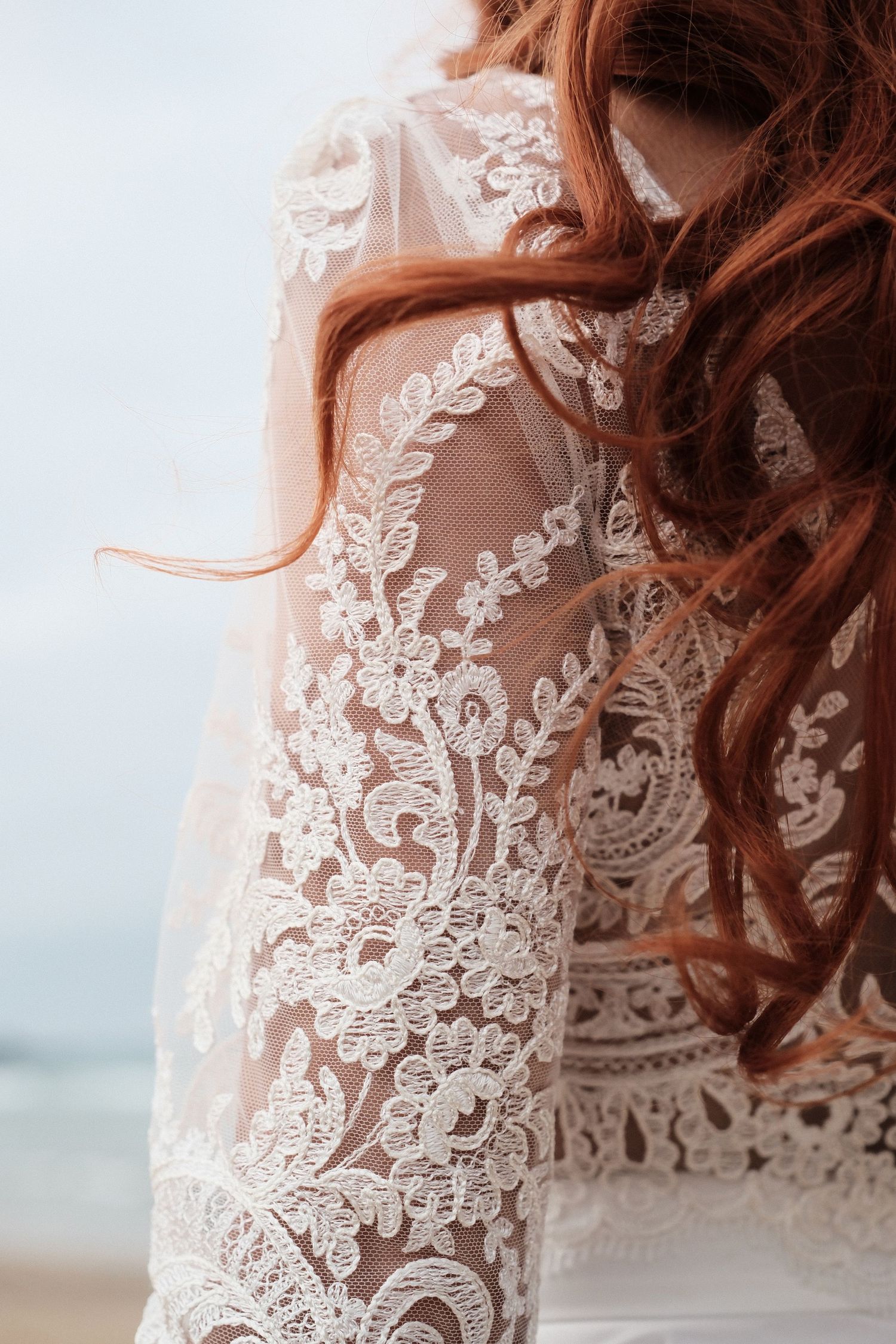 Close-up of a bride with red curly hair wearing an elegant white lace wedding dress with floral embroidery.