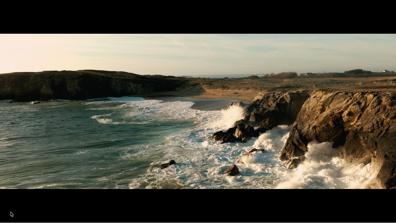Powerful ocean waves crashing against rocky cliffs along a scenic coastal landscape.