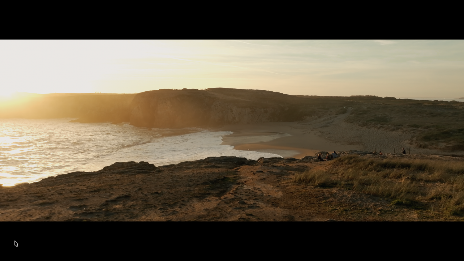 Golden sunset over a rugged coastal cliff with sandy beach and ocean waves below.