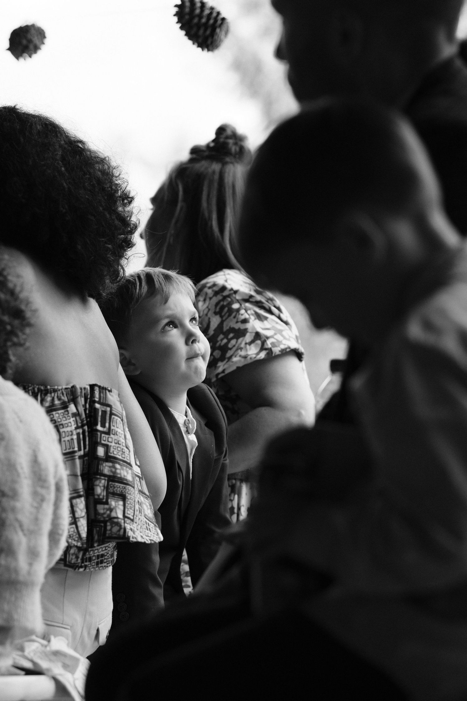 Black and white photo of a young child gazing up among wedding guests.