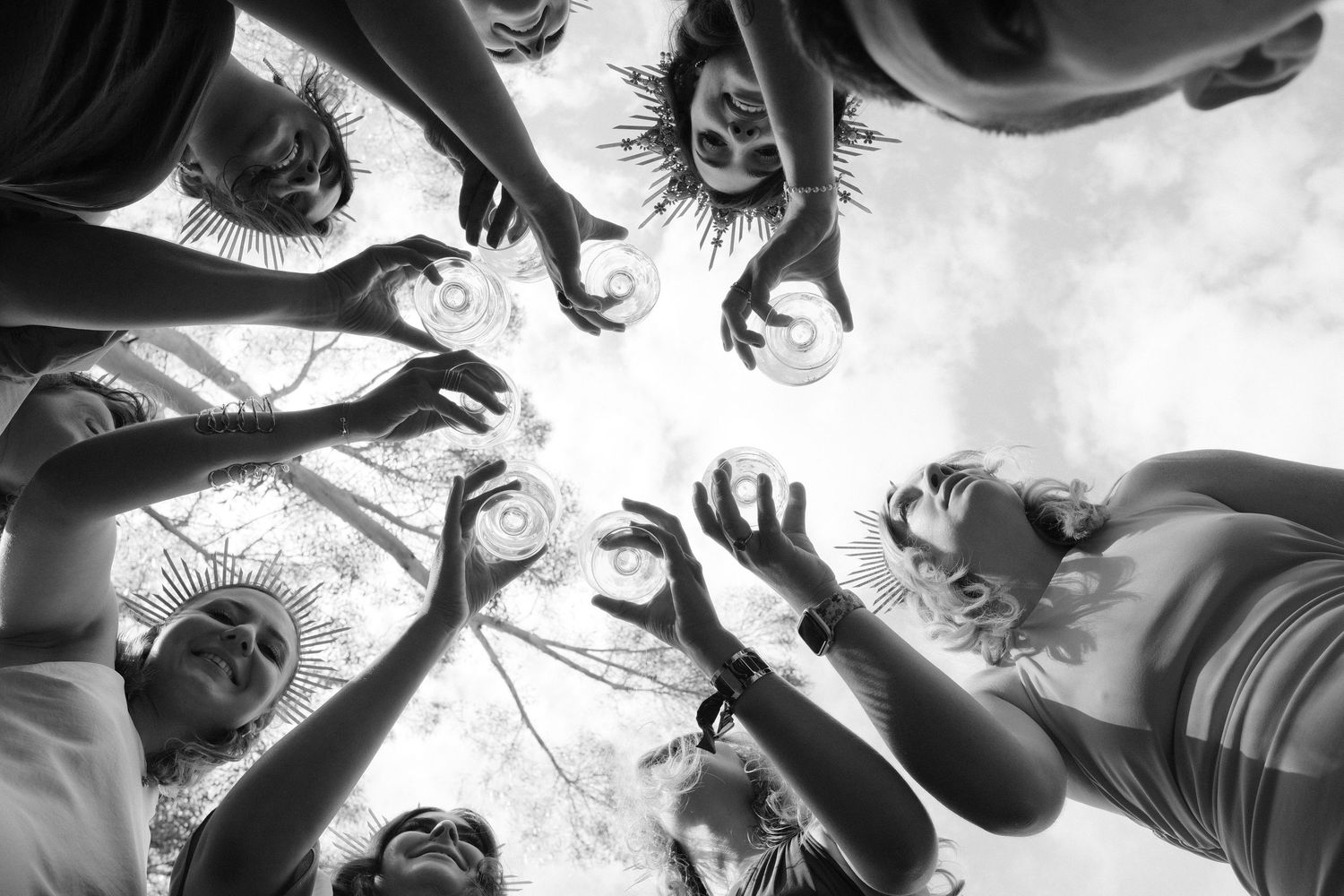 Black and white photo of a group of people reaching hands upward in a circle, viewed from below.