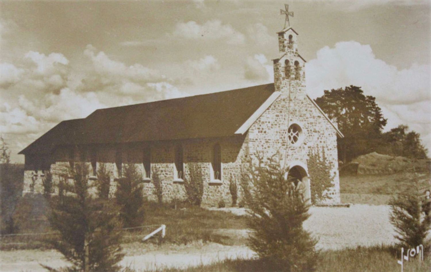 Historic stone church with bell tower and cross, surrounded by trees in a vintage sepia photograph.