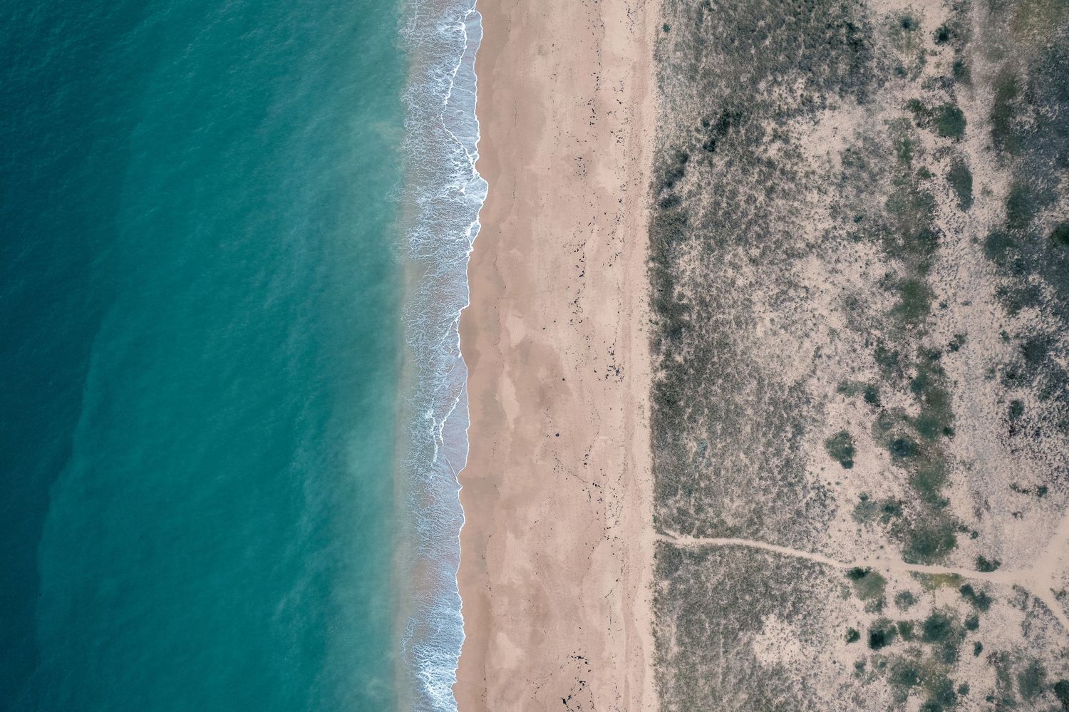 Aerial view of a sandy beach with turquoise ocean waves meeting arid scrubland terrain.