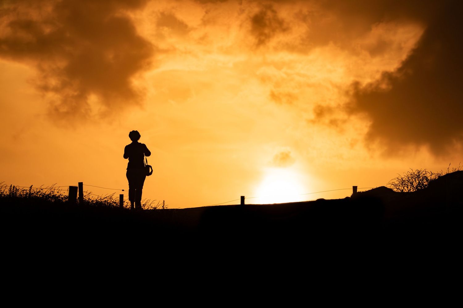 Silhouette of a person jogging against a vibrant orange sunset sky with dramatic clouds.