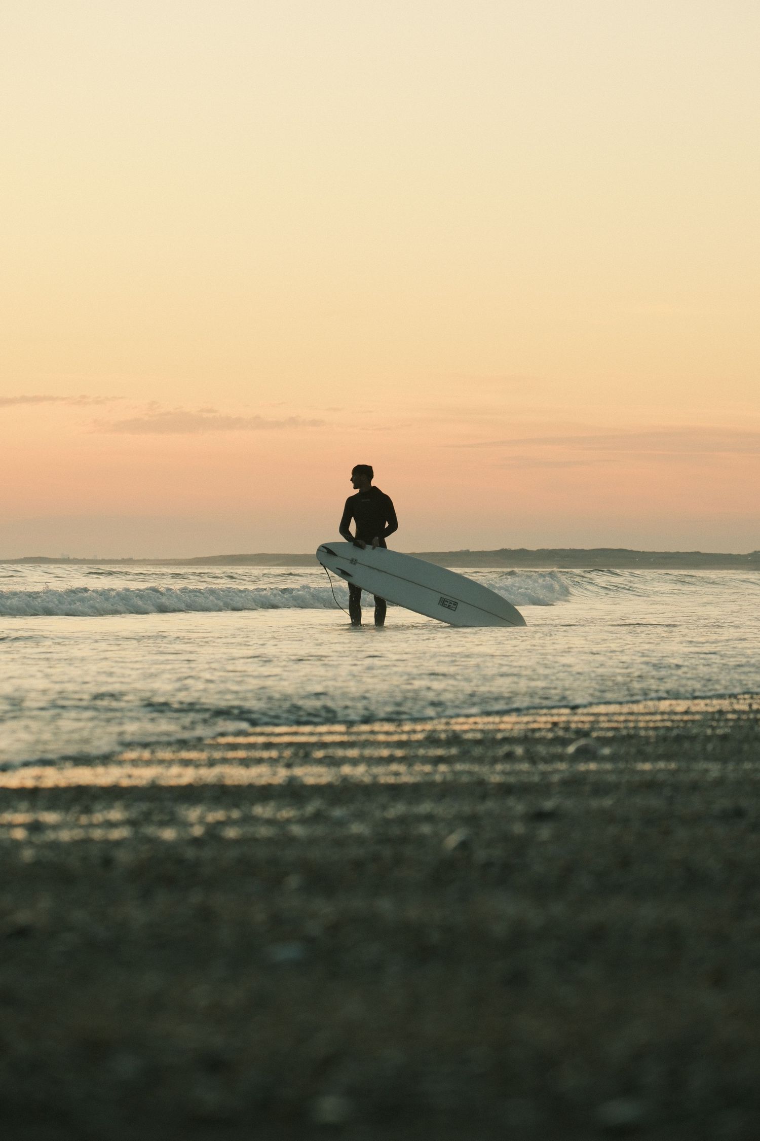 Silhouette of a surfer holding a longboard at the ocean's edge during a golden sunset.