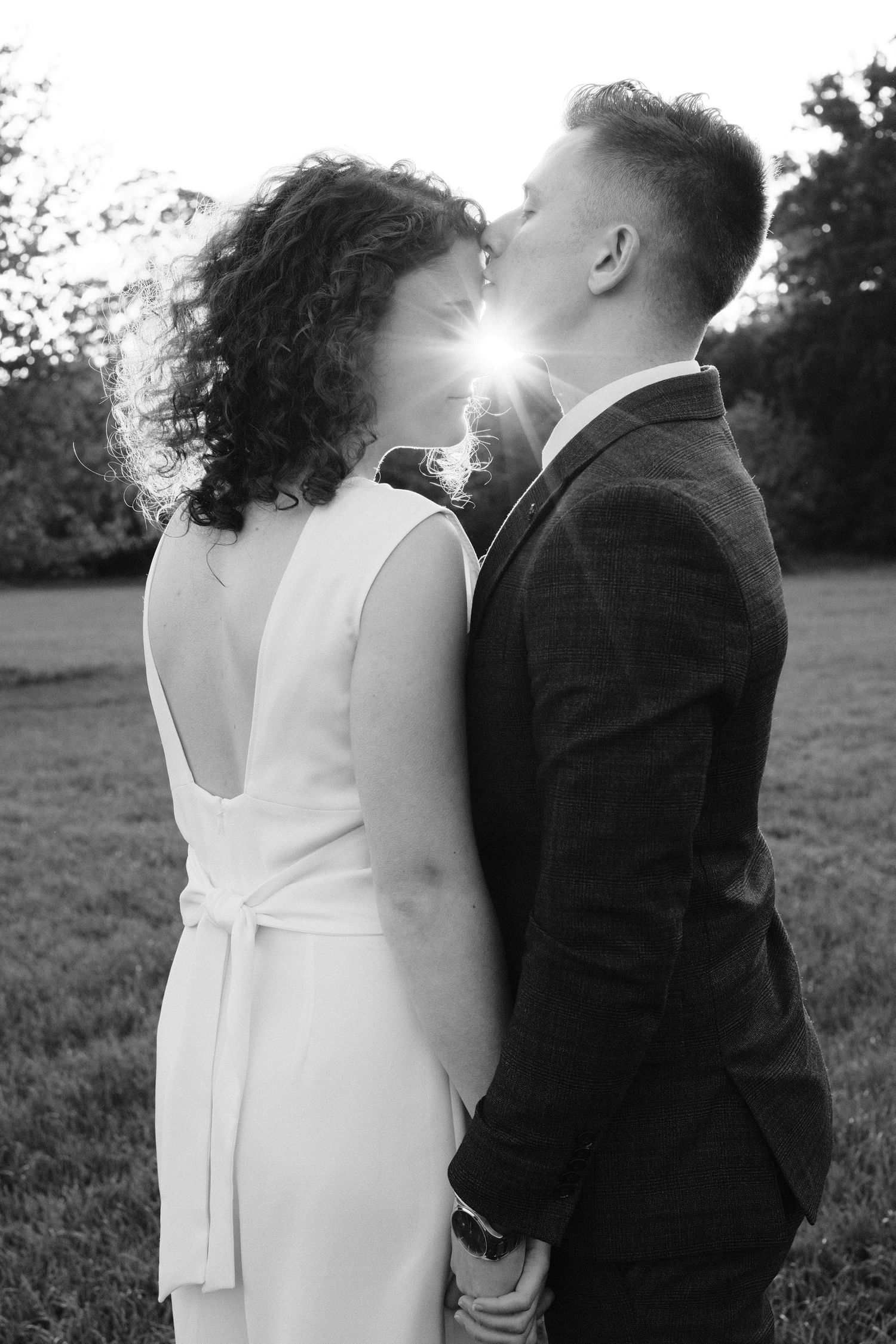 Black and white photo of bride and groom kissing with sunlight between them.