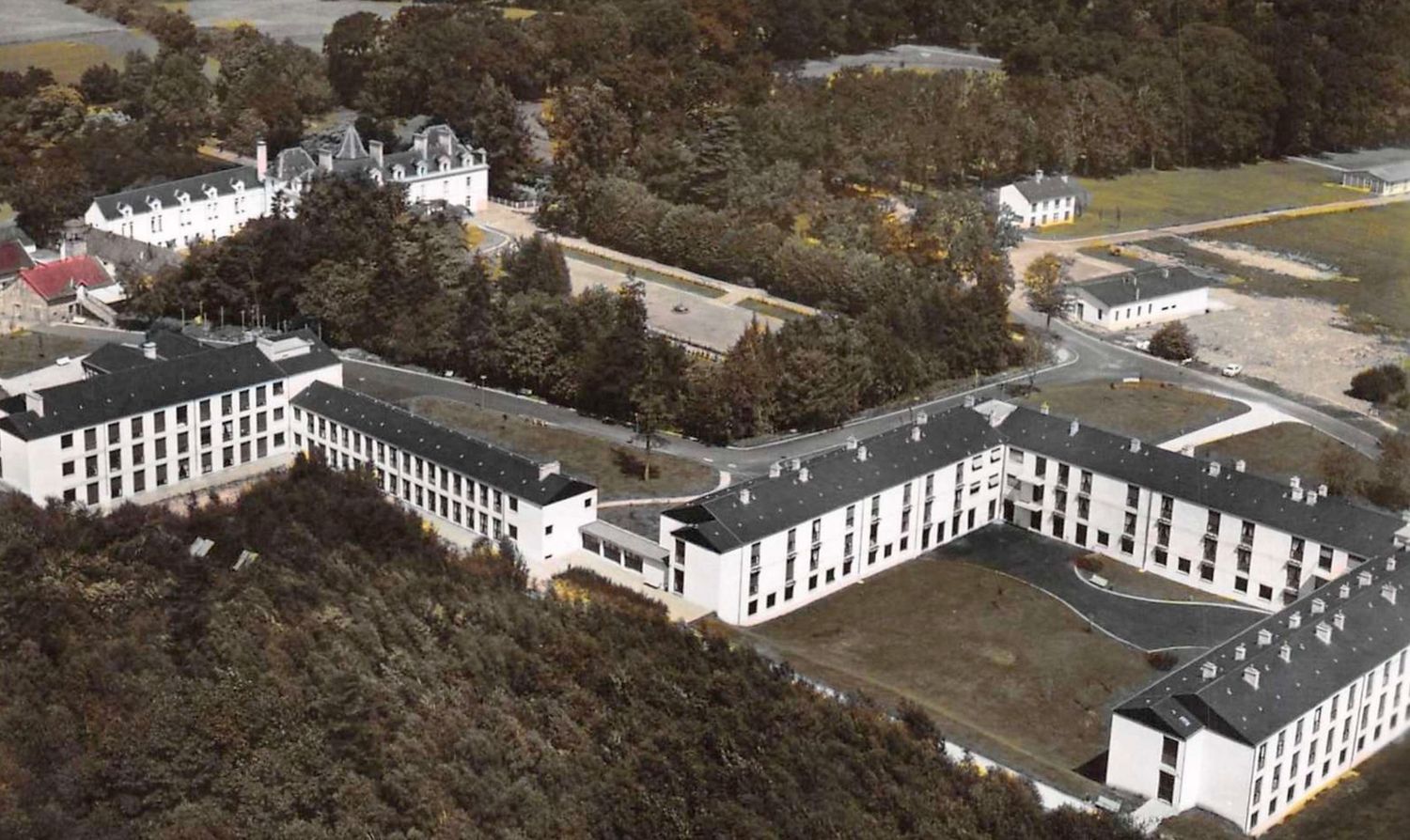 Aerial view of a large white multi-wing institutional building complex surrounded by trees.