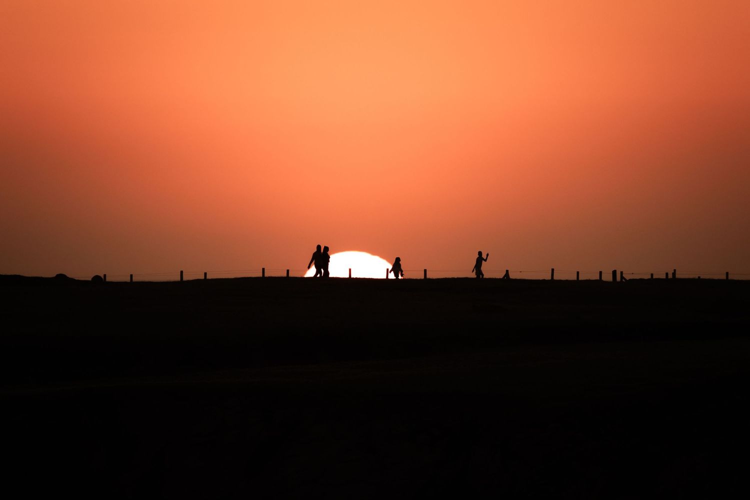 Silhouettes of people on a hilltop against a vivid orange sunset sky at dusk.