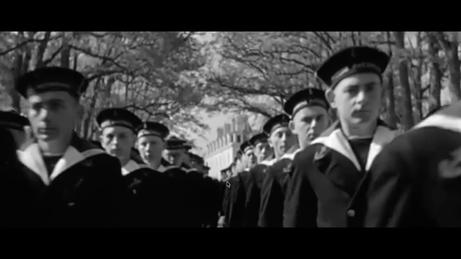 Black and white vintage photo of naval cadets marching in uniform through a tree-lined path.