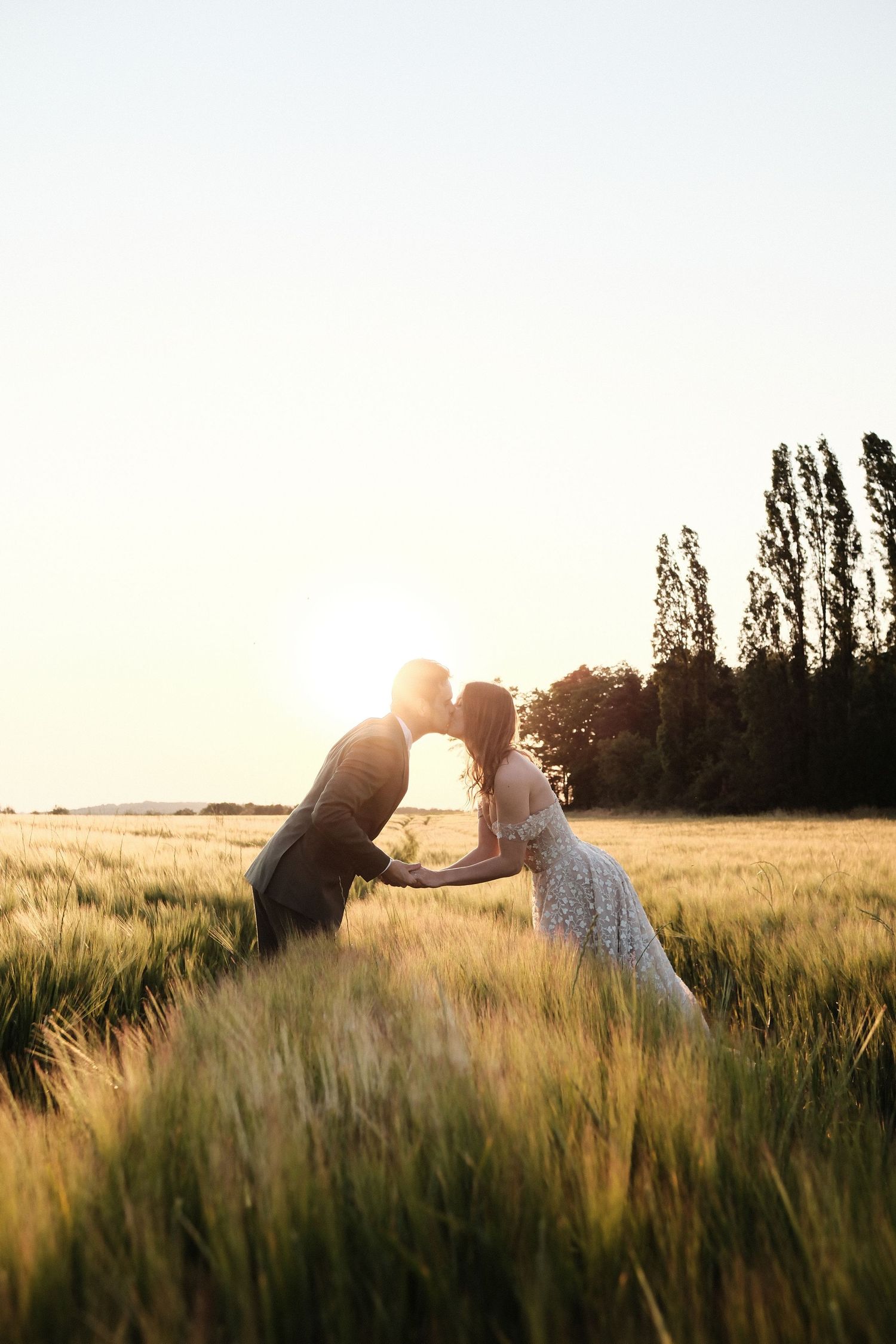 Wedding couple sharing a romantic kiss in a golden wheat field at sunset.