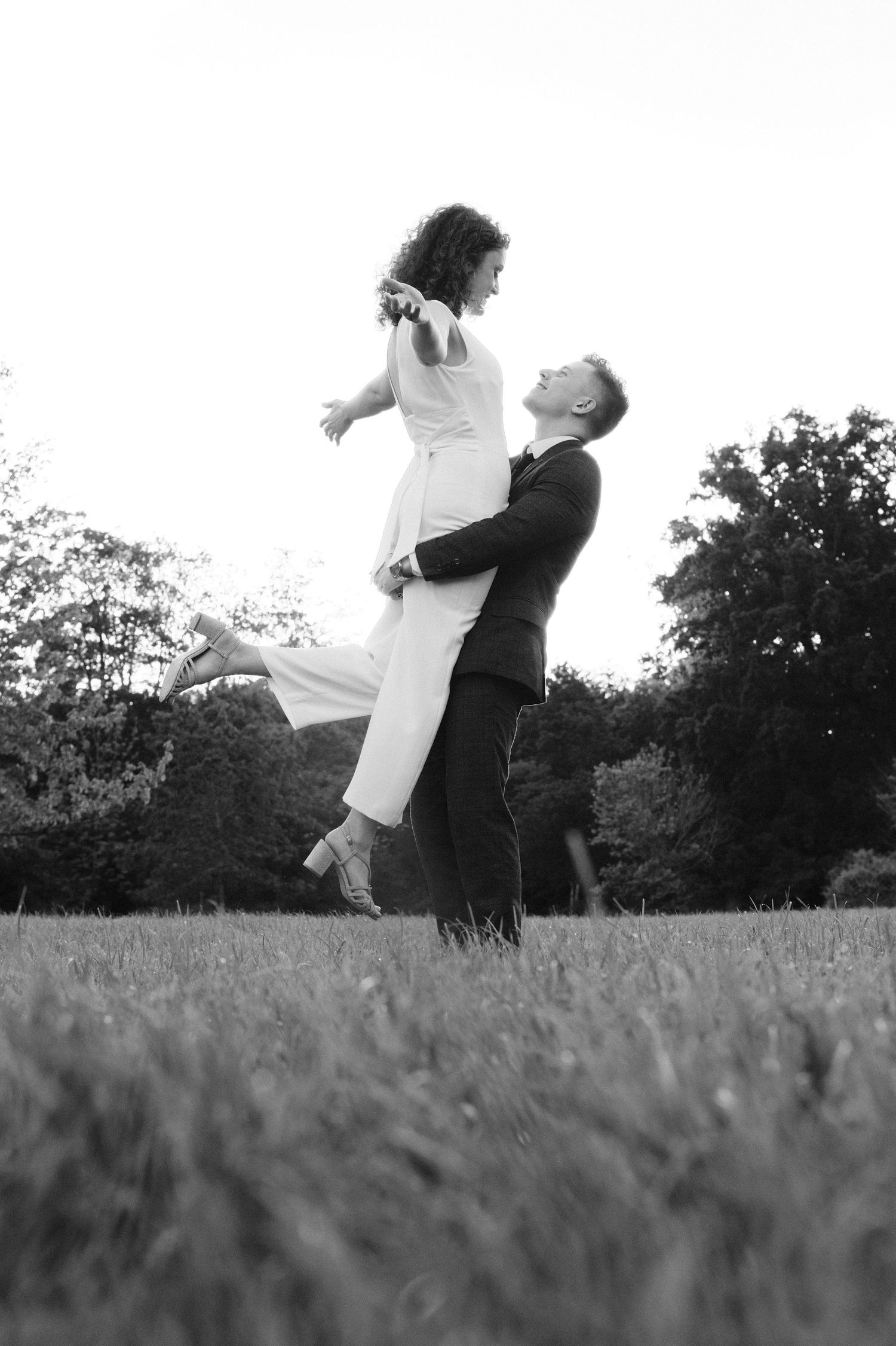 Black and white photo of groom lifting bride joyfully in an outdoor park.