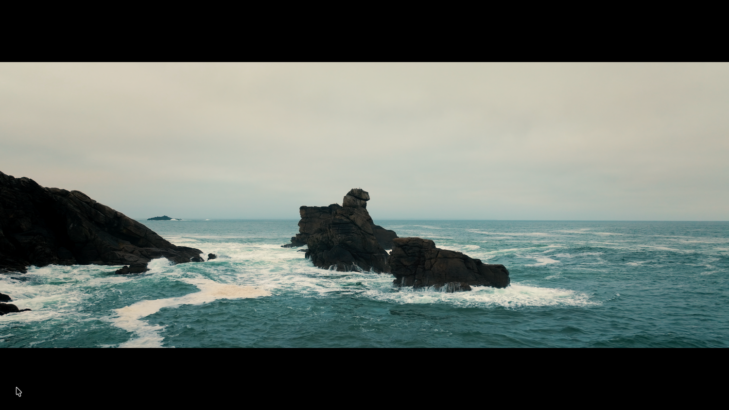 Lone rocky sea stack surrounded by turquoise ocean waves under an overcast sky.