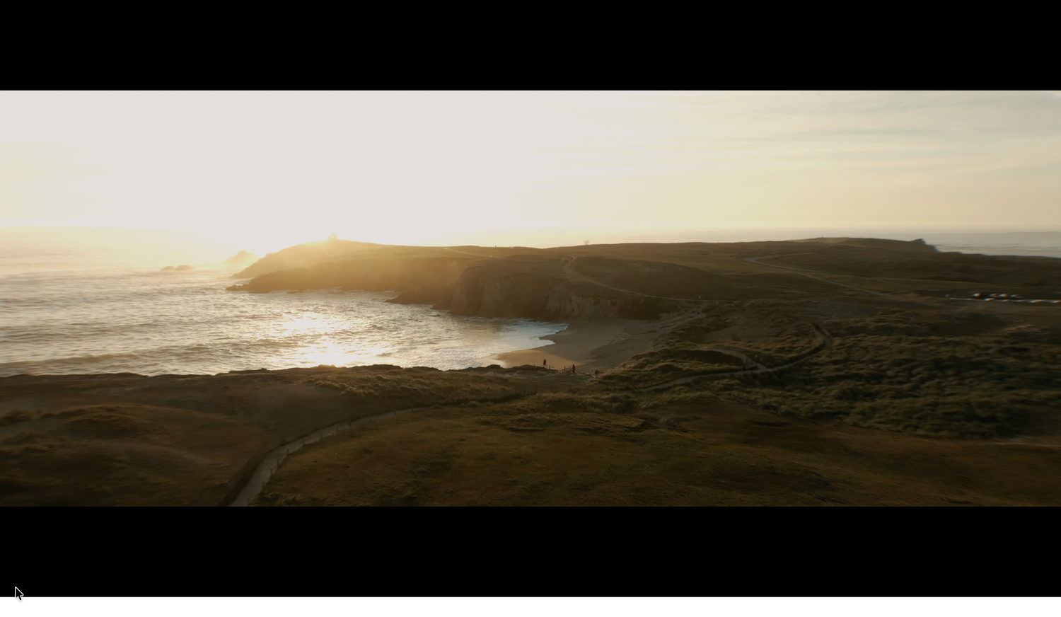 Aerial view of golden sunset over coastal cliffs and green hillside with winding road below.