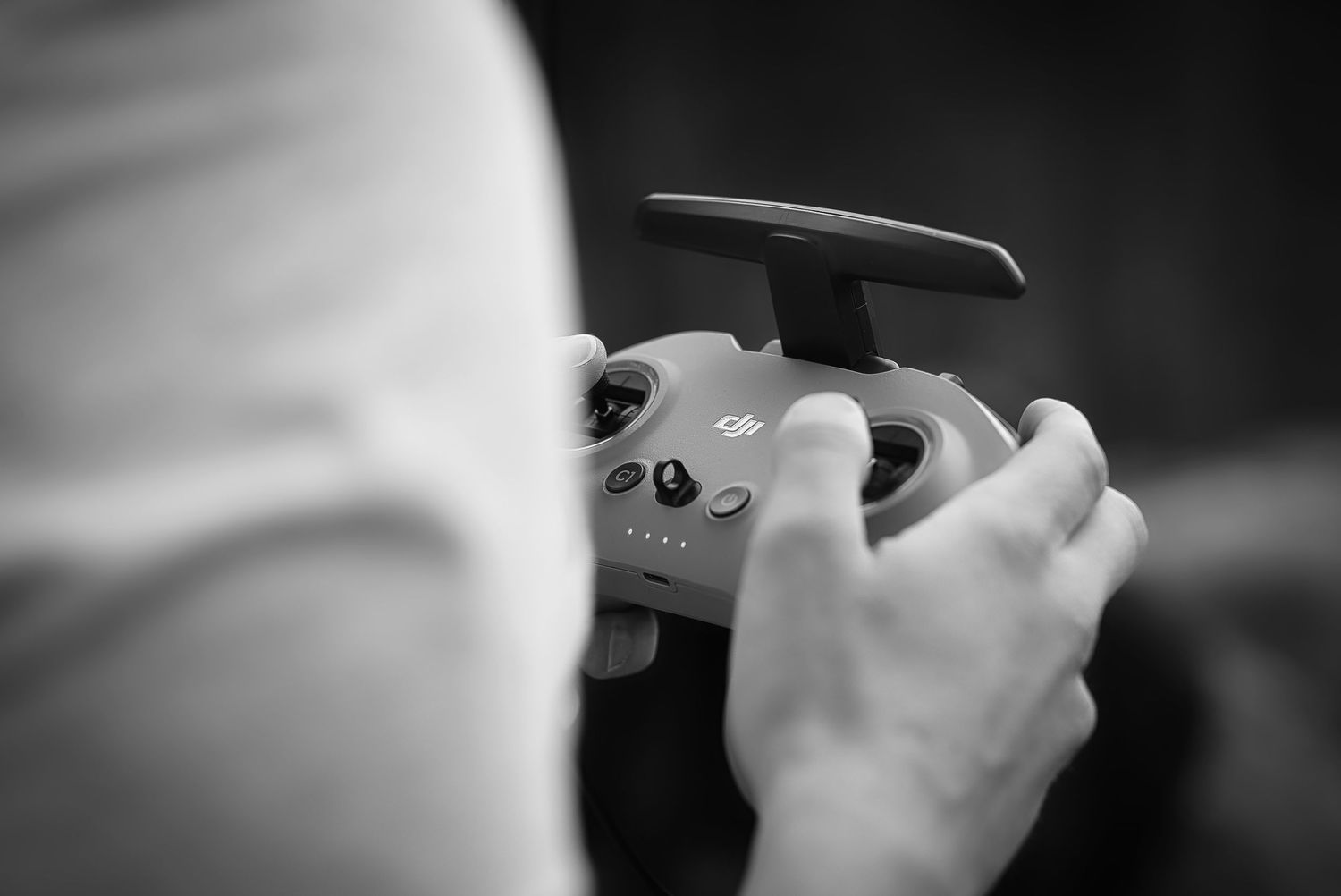 Black and white close-up of hands holding a DJI drone remote controller outdoors.