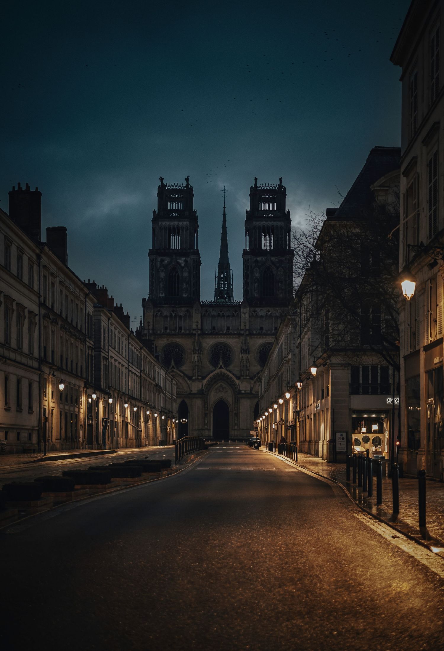 Gothic cathedral with twin towers illuminated at night on a empty cobblestone street in Orleans, France.