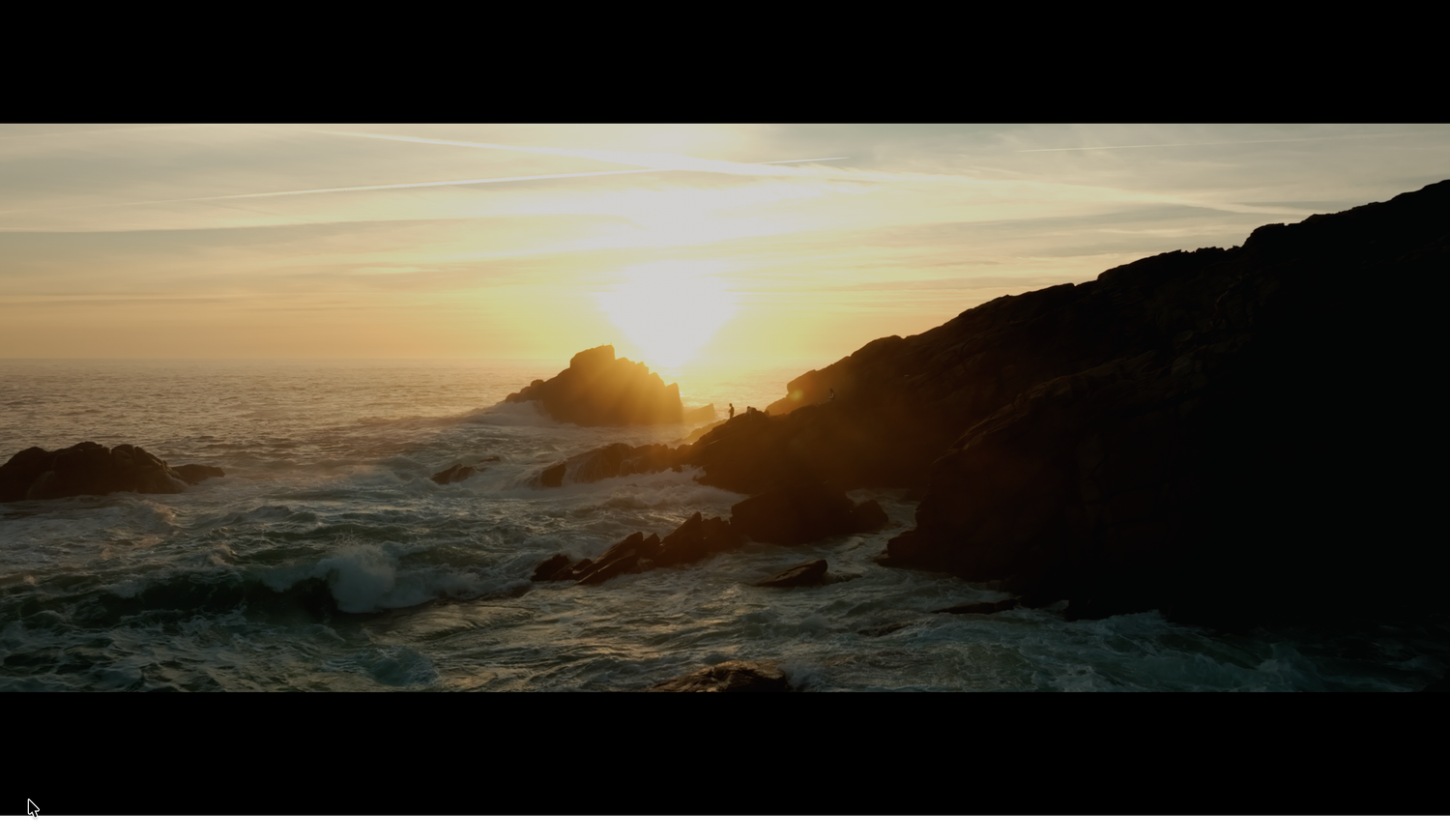 Golden sunset over rocky ocean coastline with waves crashing against dark silhouetted rocks.