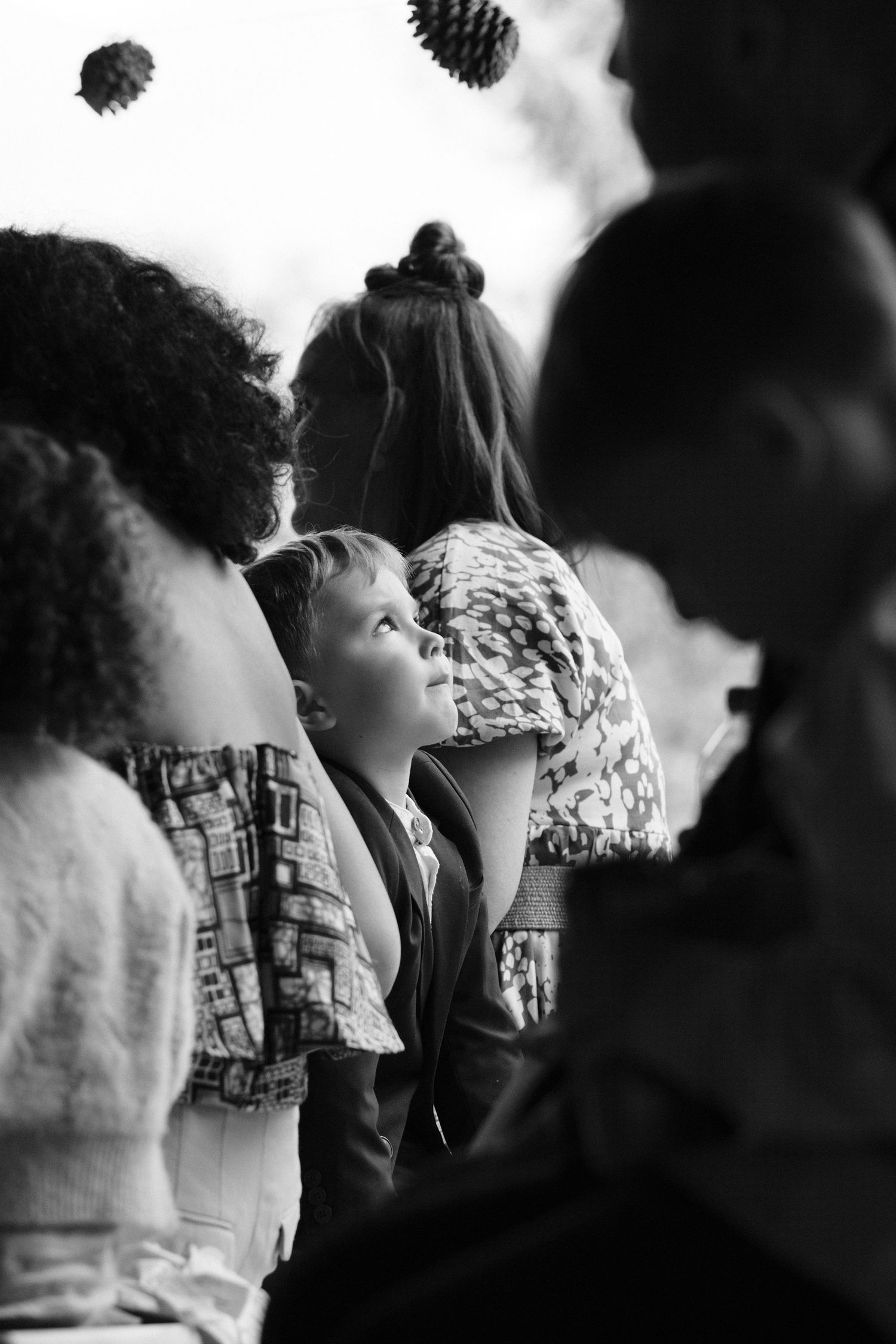 Black and white image of a young boy looking up surrounded by wedding guests.