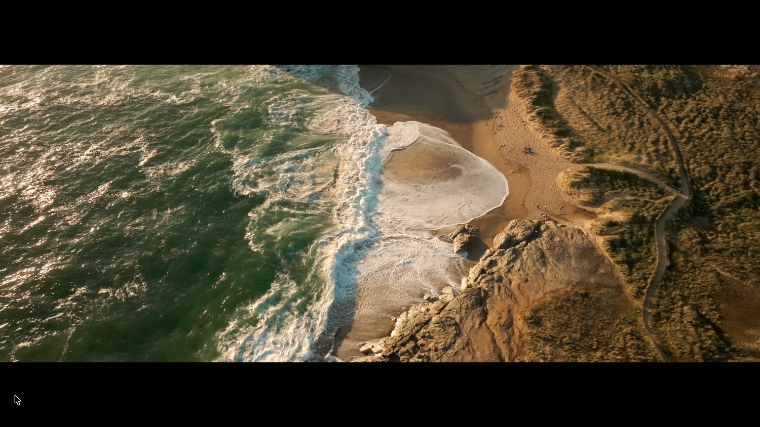 Aerial view of ocean waves meeting a sandy beach along a rocky coastline.