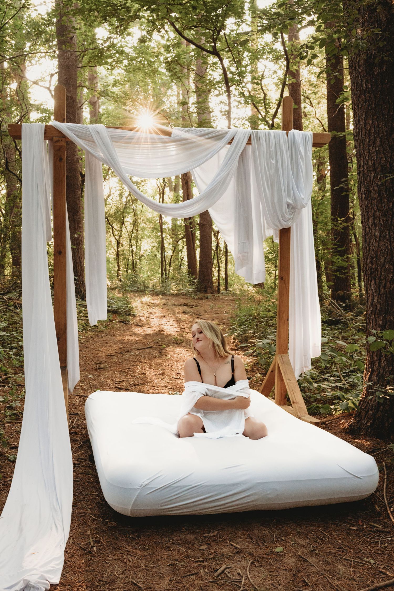Outdoor boudoir photography set featuring a bed surrounded by forest scenery.